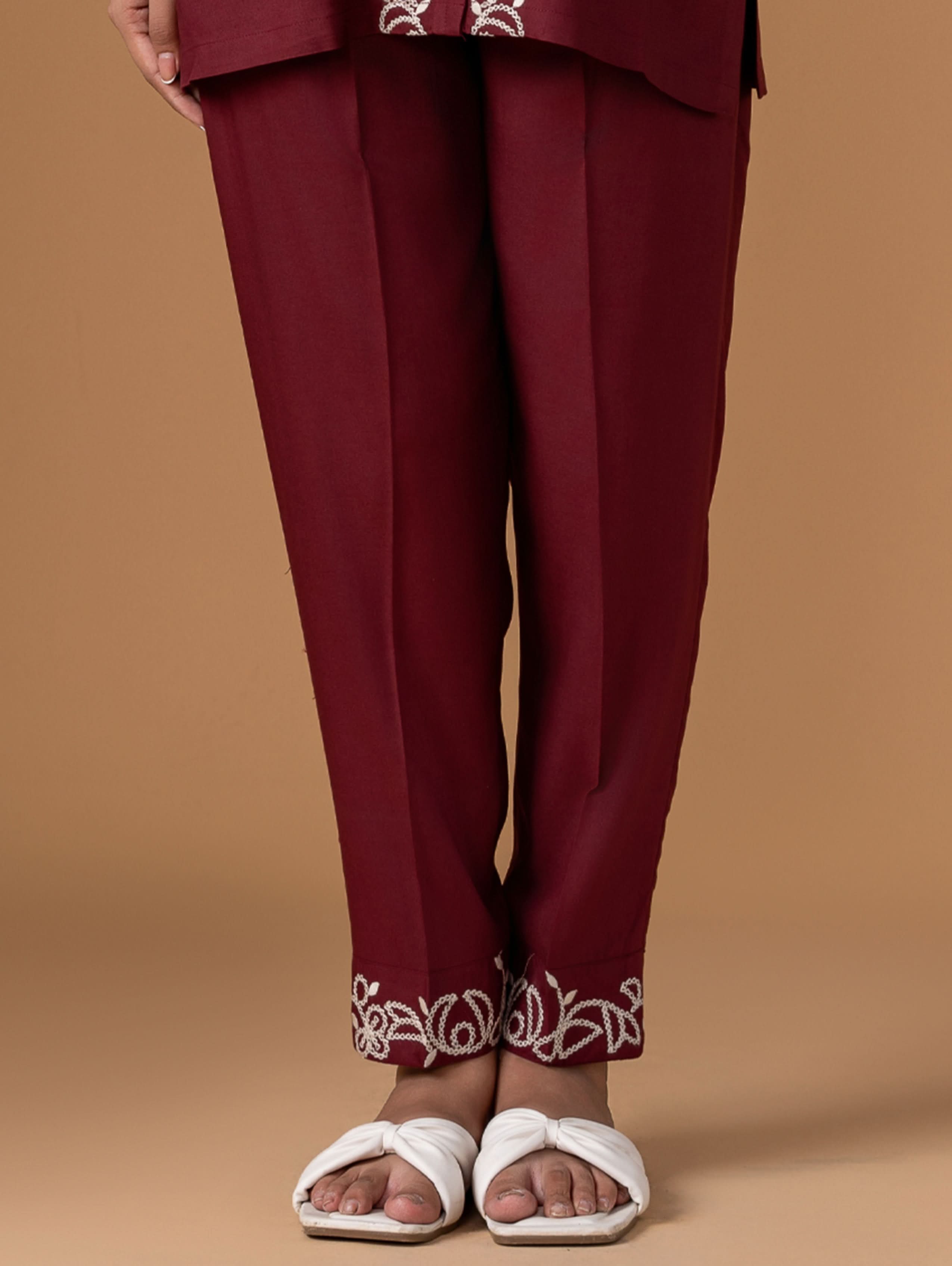 Maroon pants with white embroidery at the bottom worn by a person on a brown background
