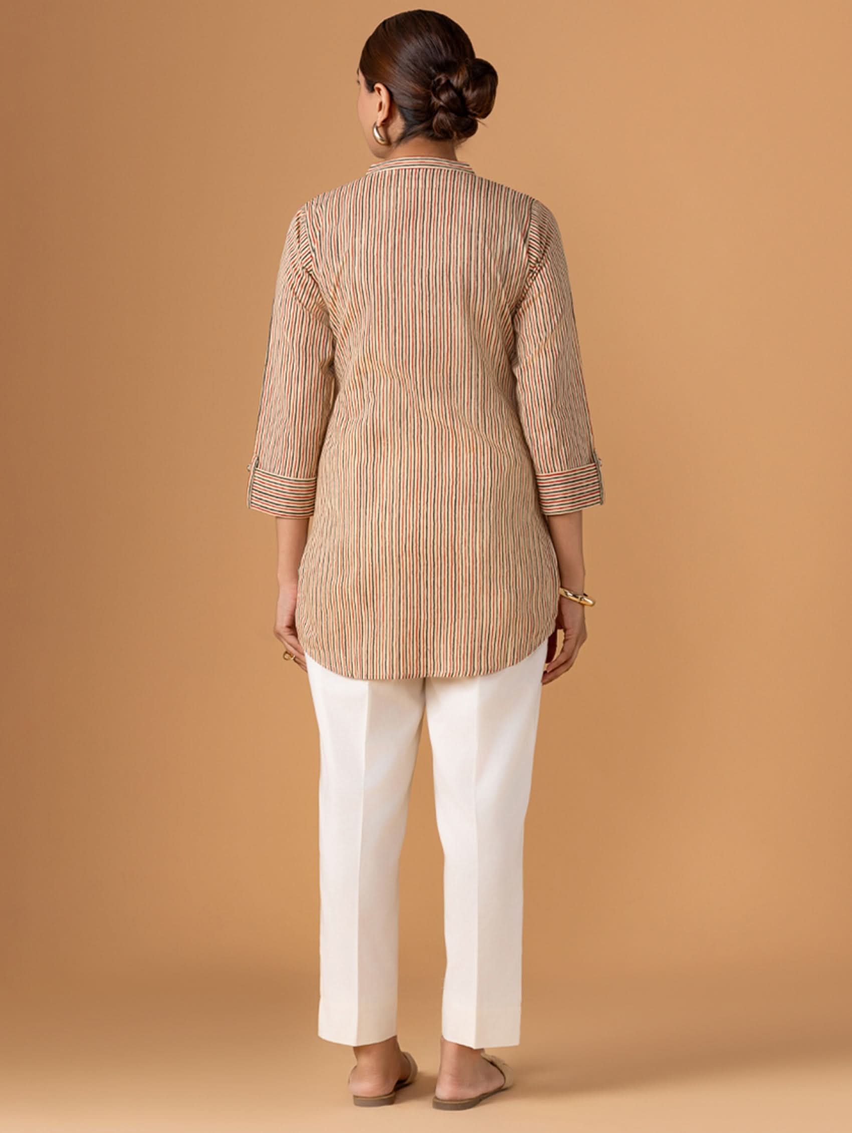 Woman wearing a striped beige and brown kurta with white pants against a beige background