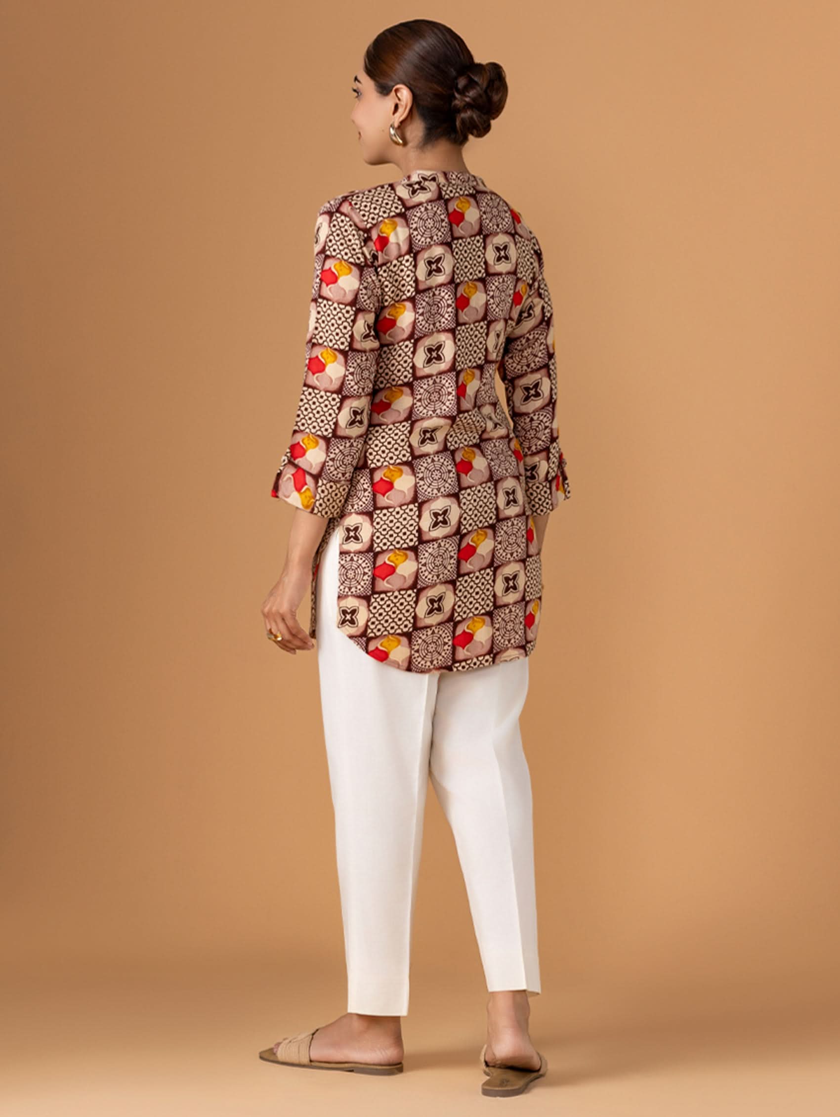 Woman wearing a patterned top and white pants on a beige background