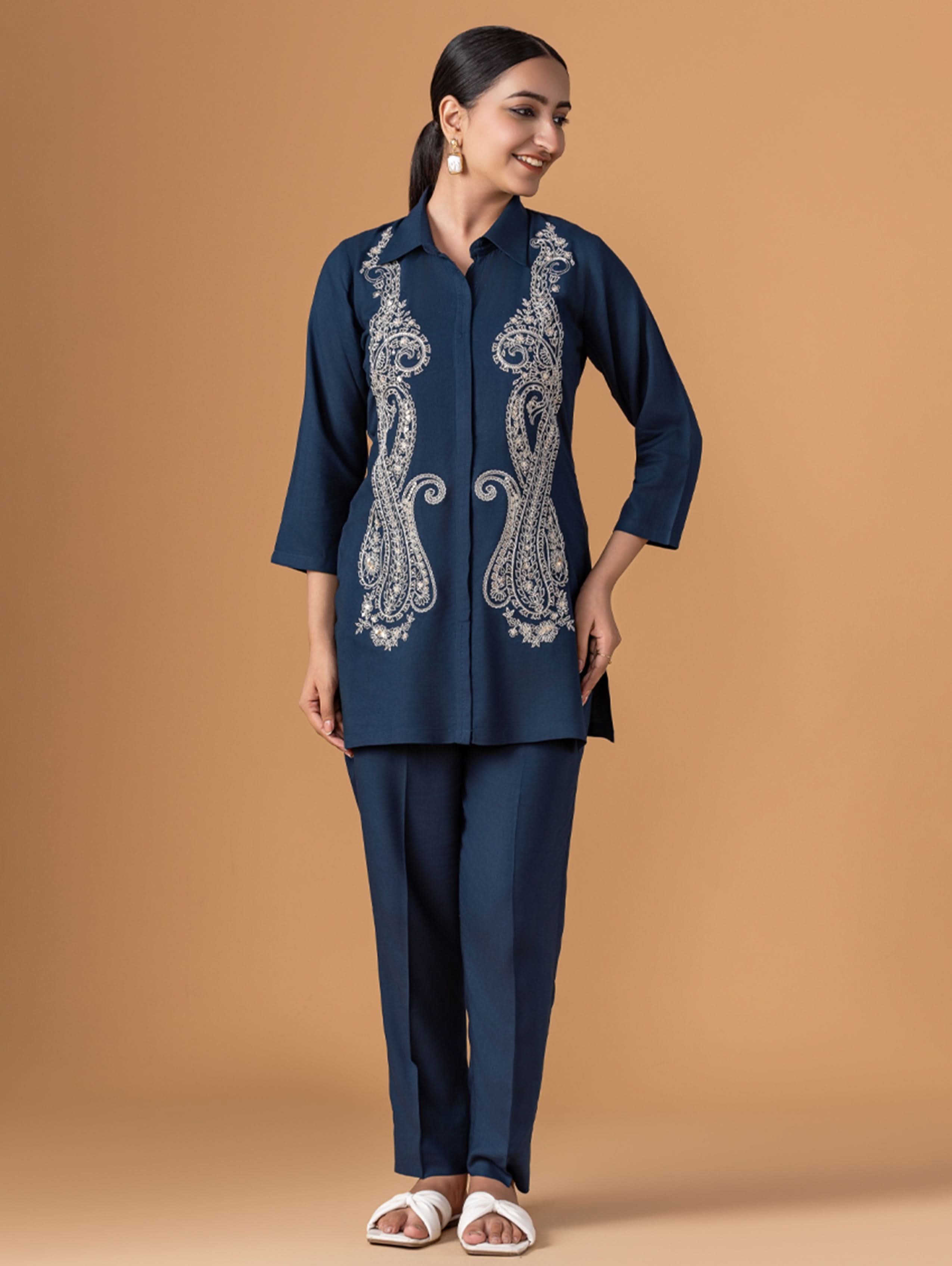 Woman wearing a navy blue outfit with intricate white embroidery on a brown background
