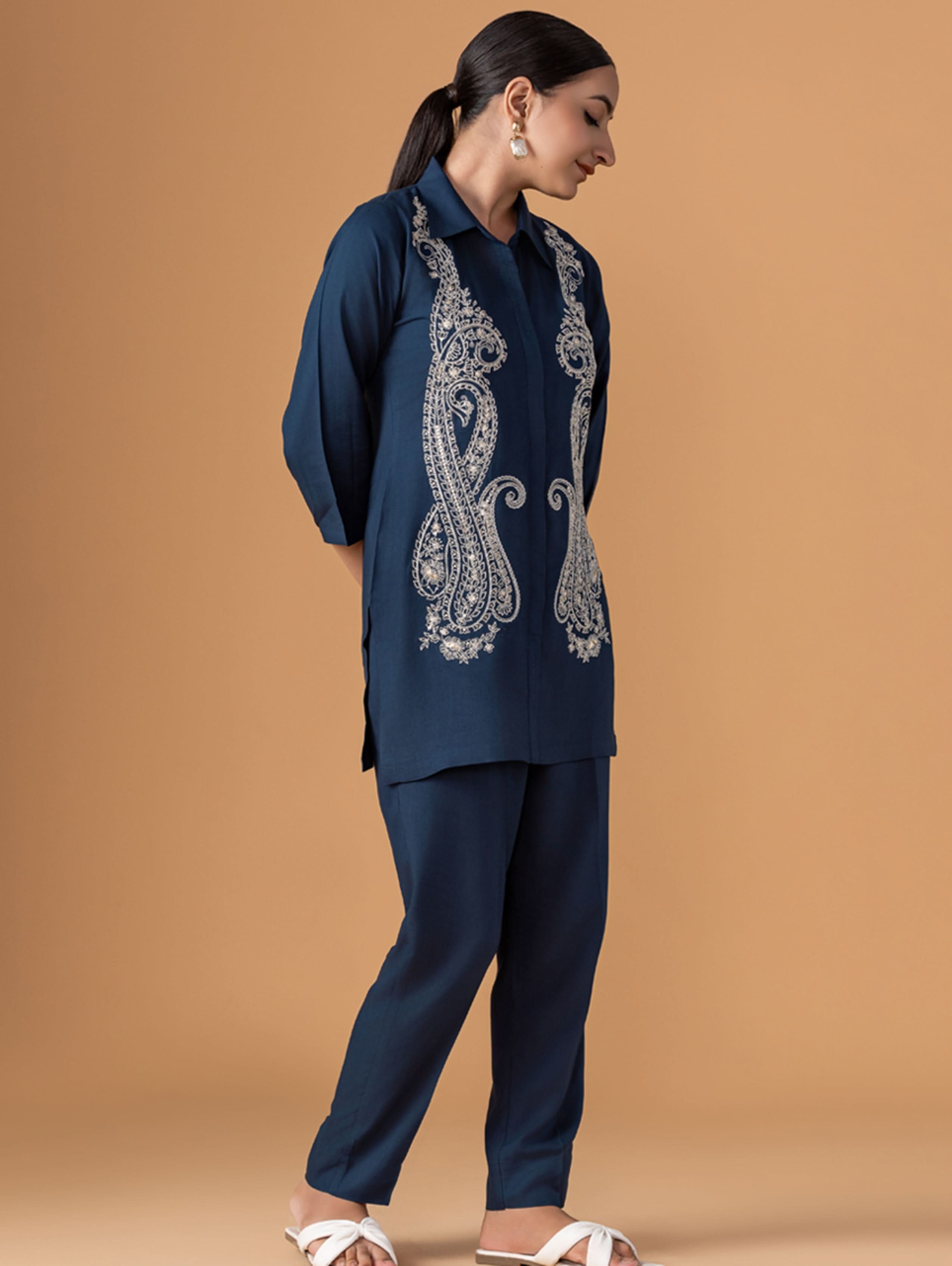 Woman wearing a navy blue embroidered outfit on a brown background