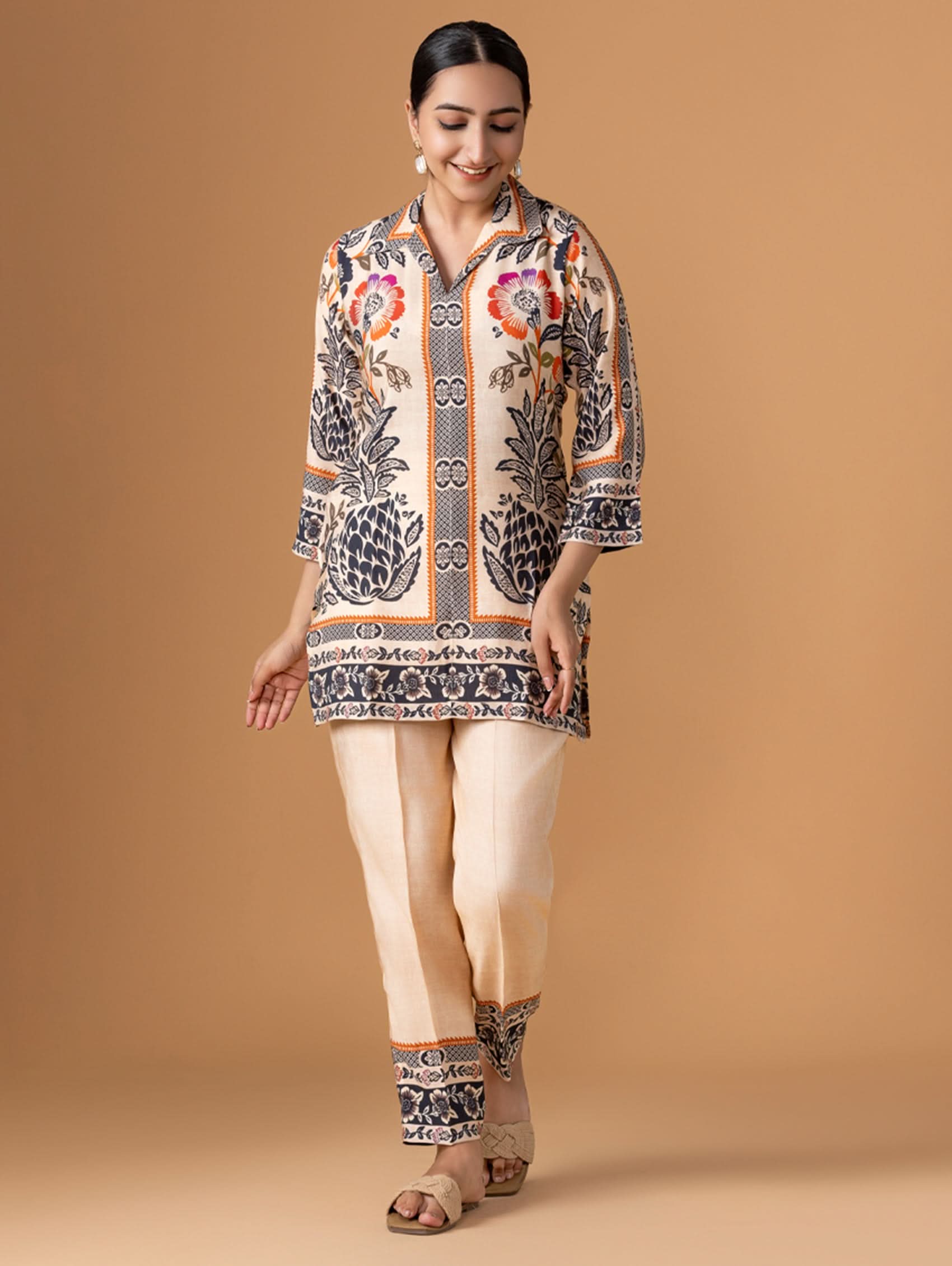 Woman wearing a patterned shirt and beige pants on a brown background