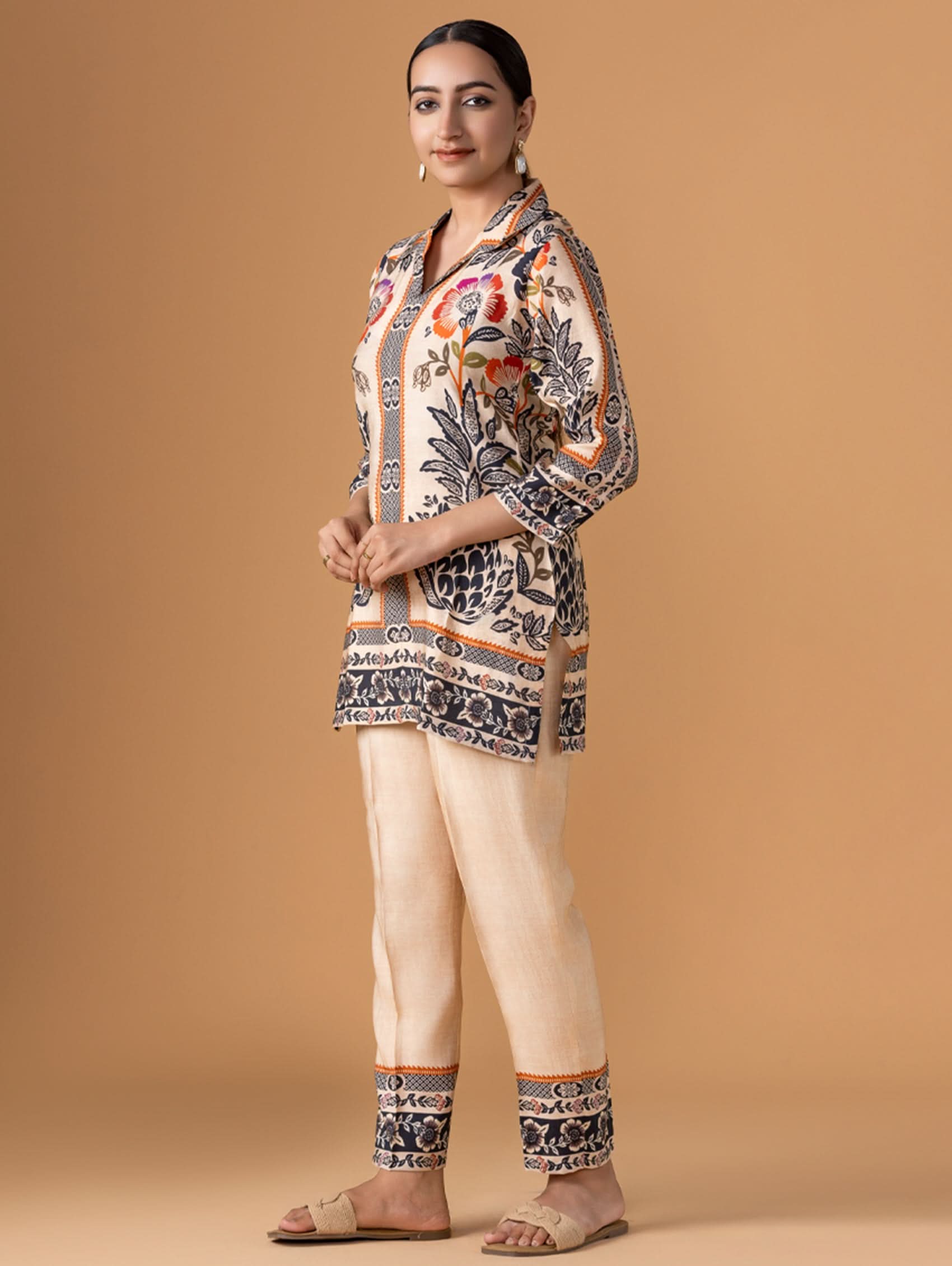 Woman wearing a patterned top and beige pants on a brown background