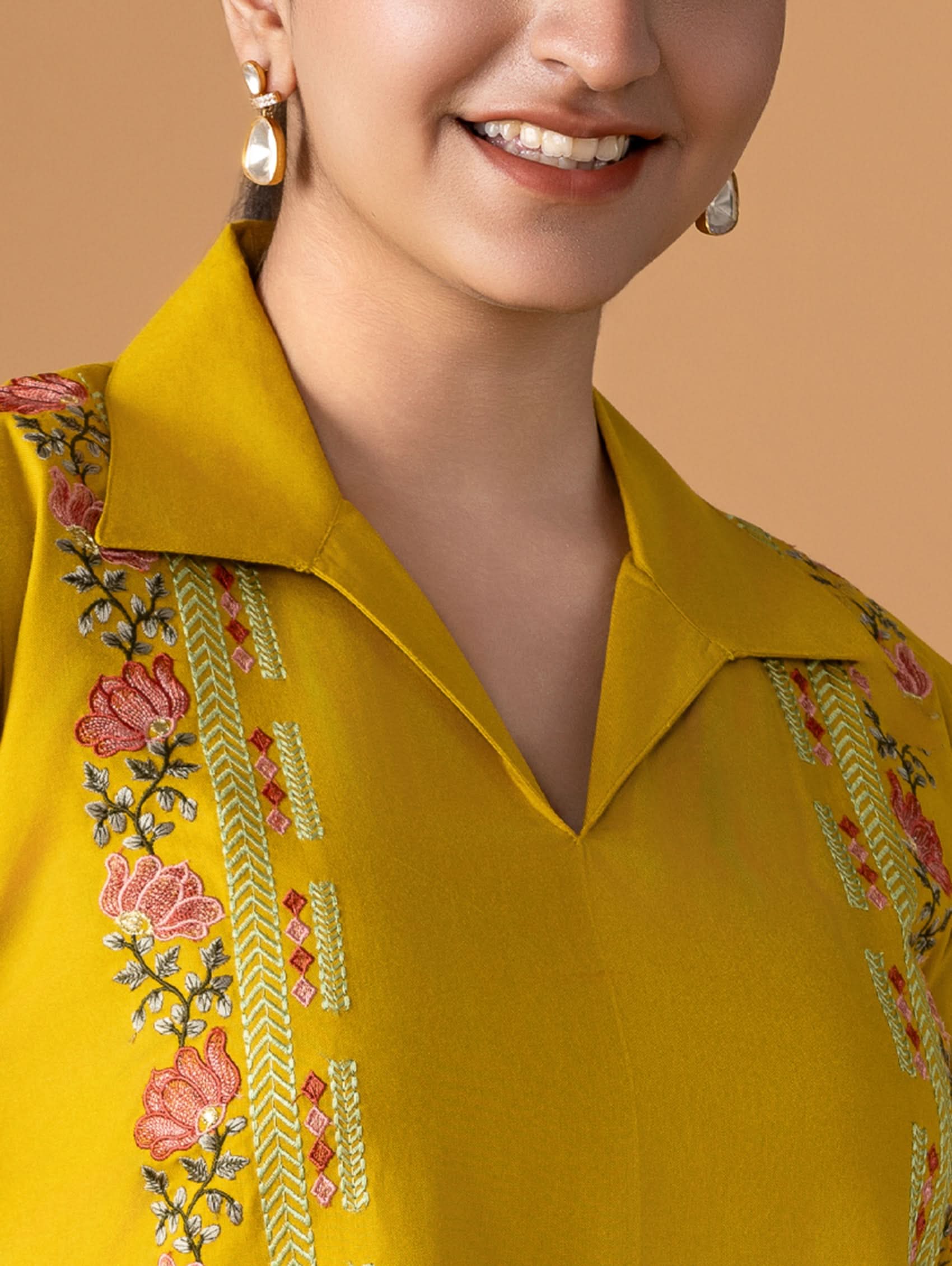 Close-up of a person wearing a yellow embroidered shirt with a beige background