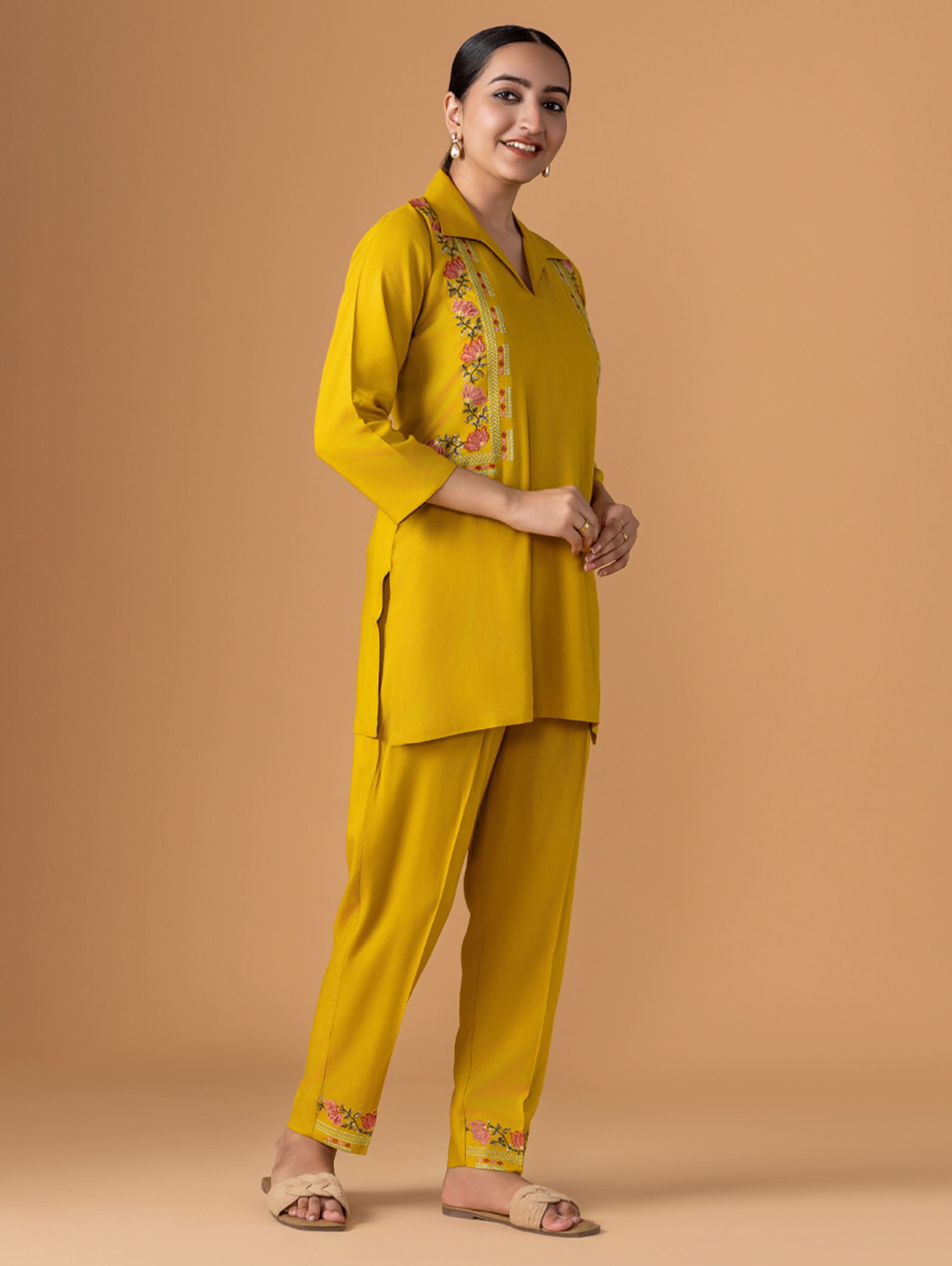 Woman wearing a yellow traditional outfit with floral embroidery on a beige background