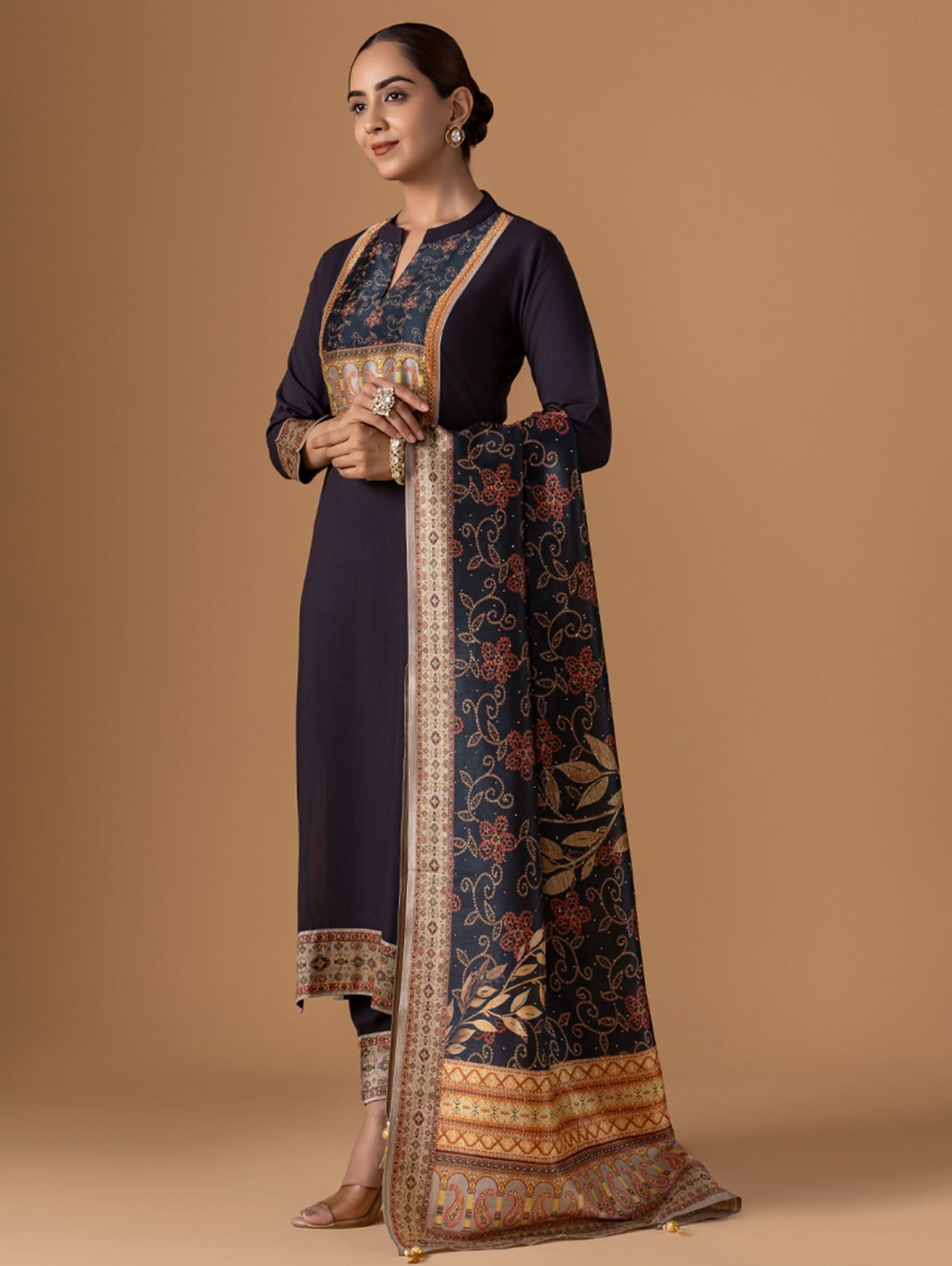 Woman wearing a traditional outfit with a dark blue kurta and patterned dupatta on a beige background
