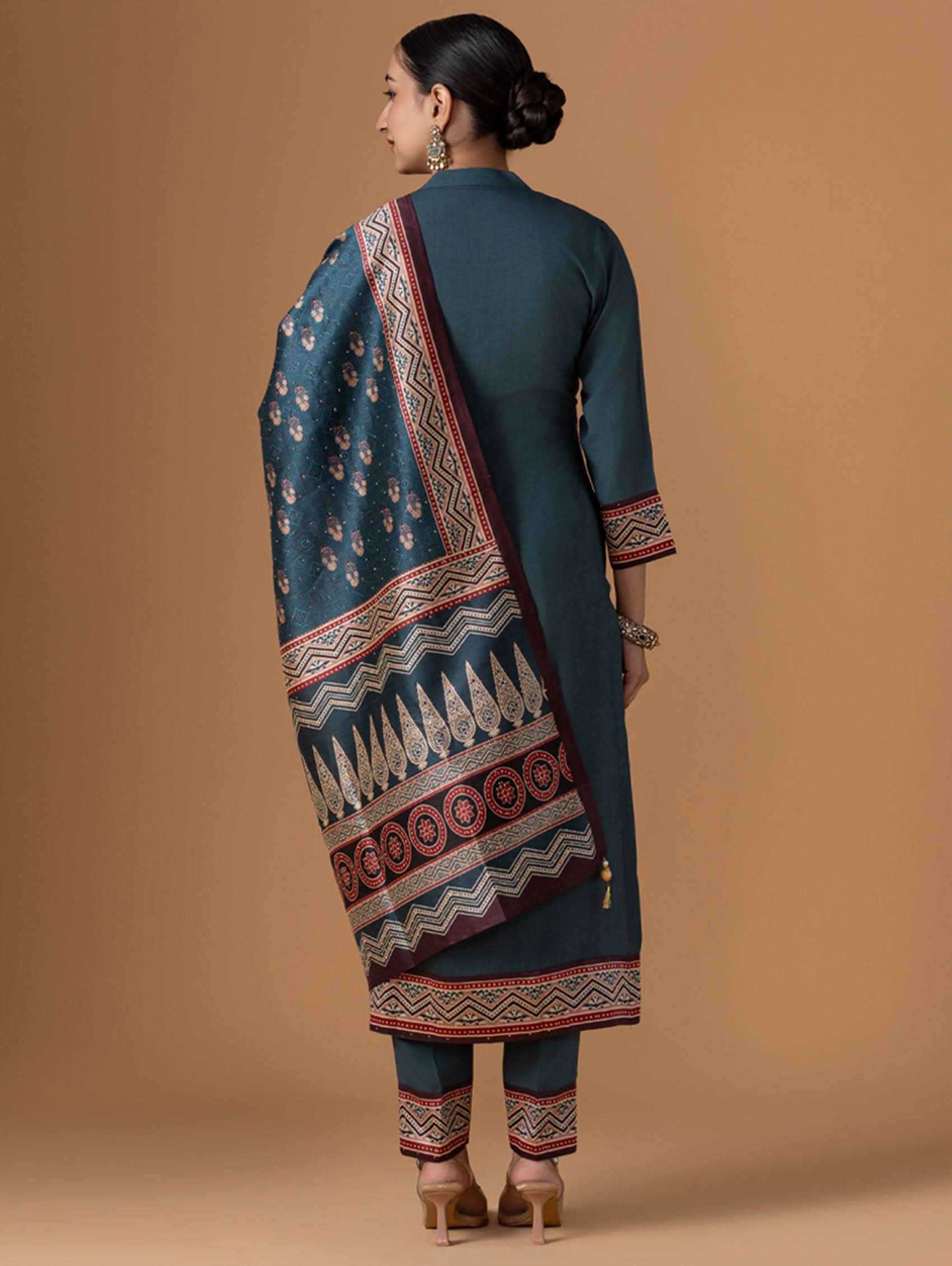 Woman wearing a traditional outfit with a patterned dupatta against a beige background