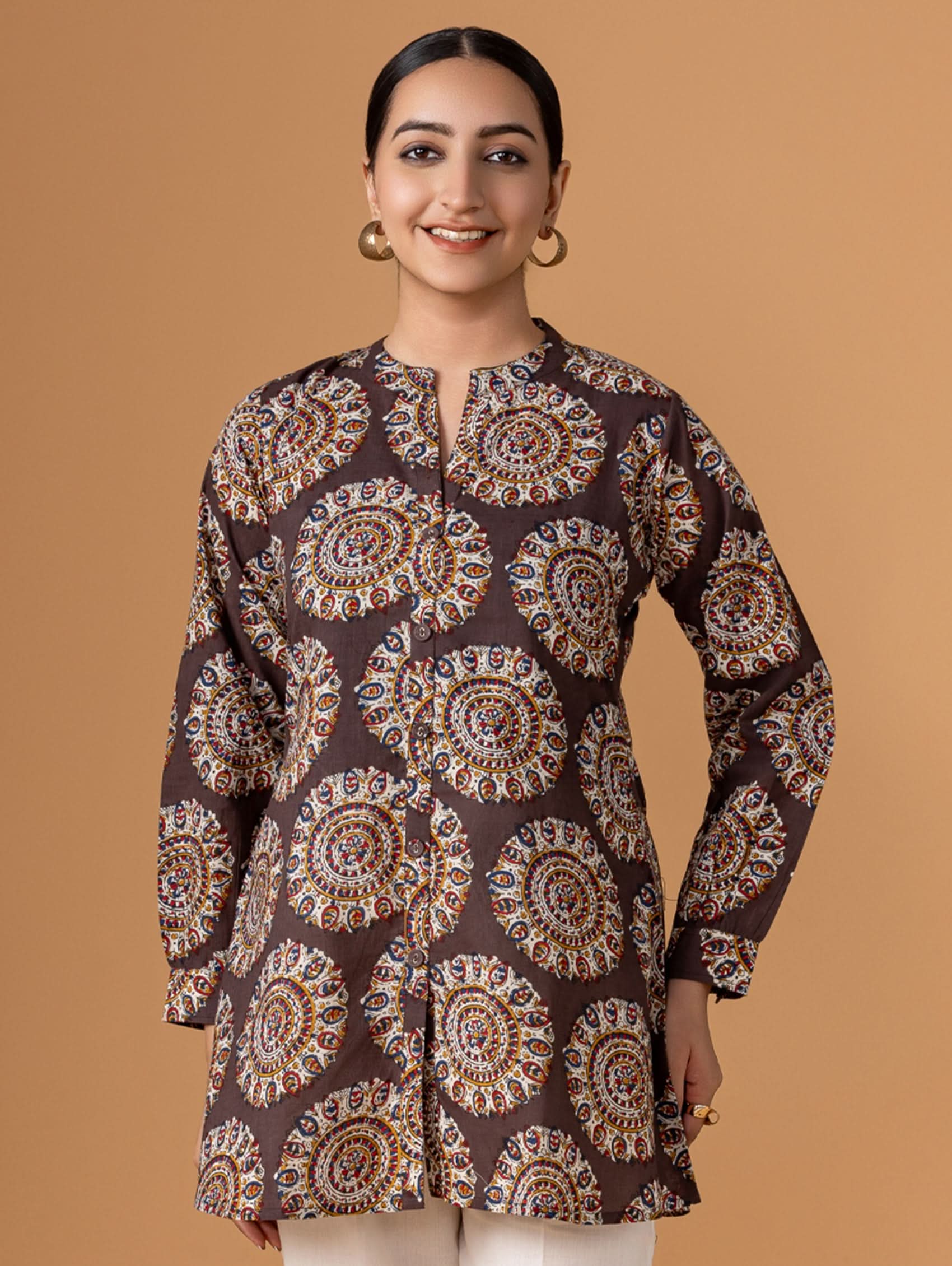 Woman wearing a patterned brown kurta against a beige background
