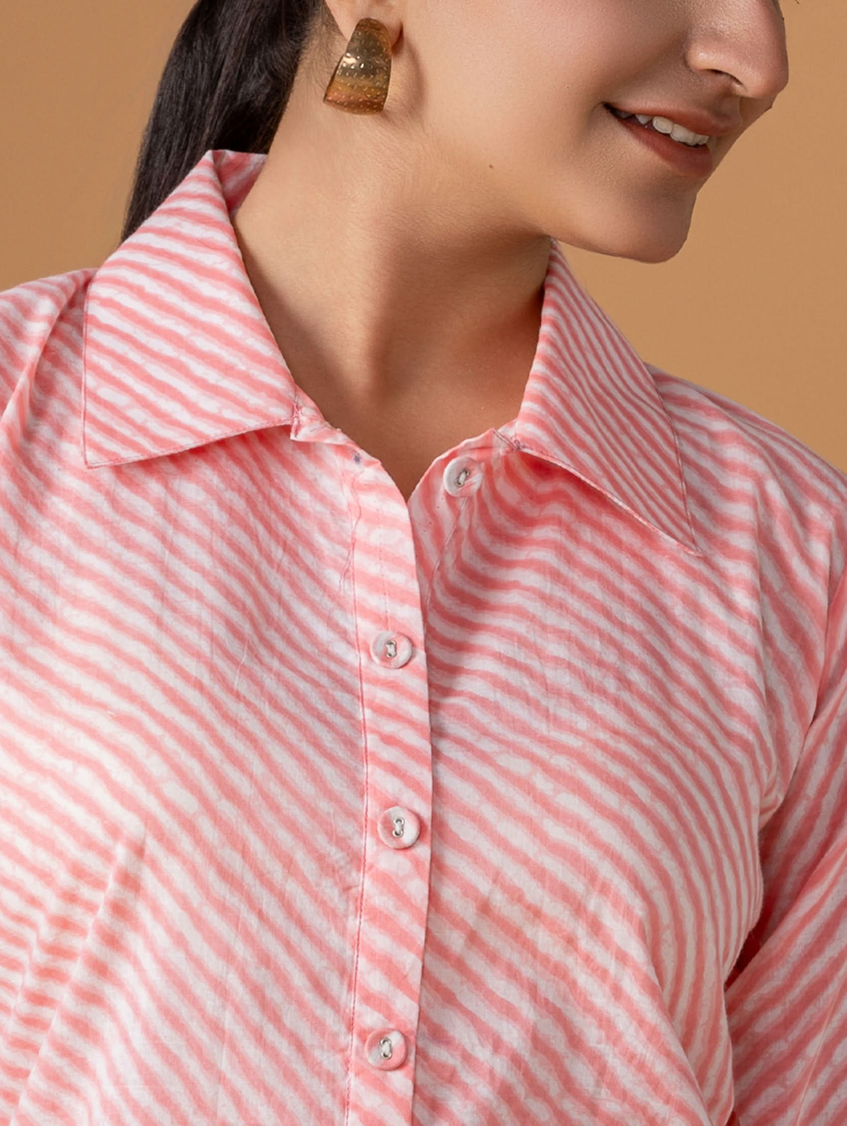 Close-up of a person wearing a pink and white striped shirt against a beige background