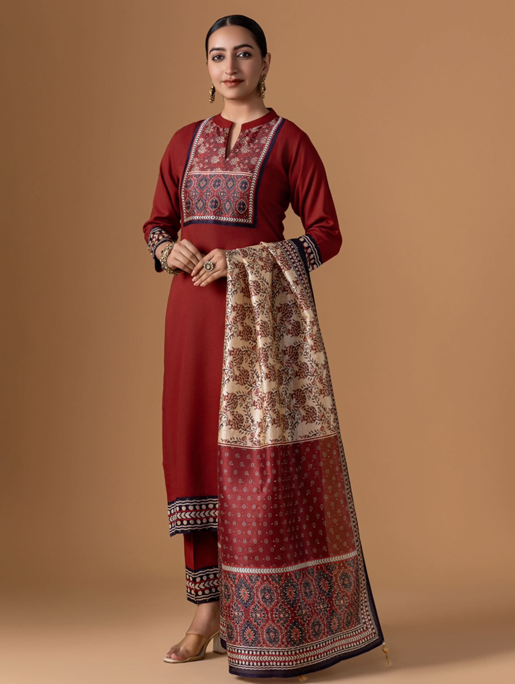 Woman wearing a red traditional outfit with patterned dupatta against a beige background