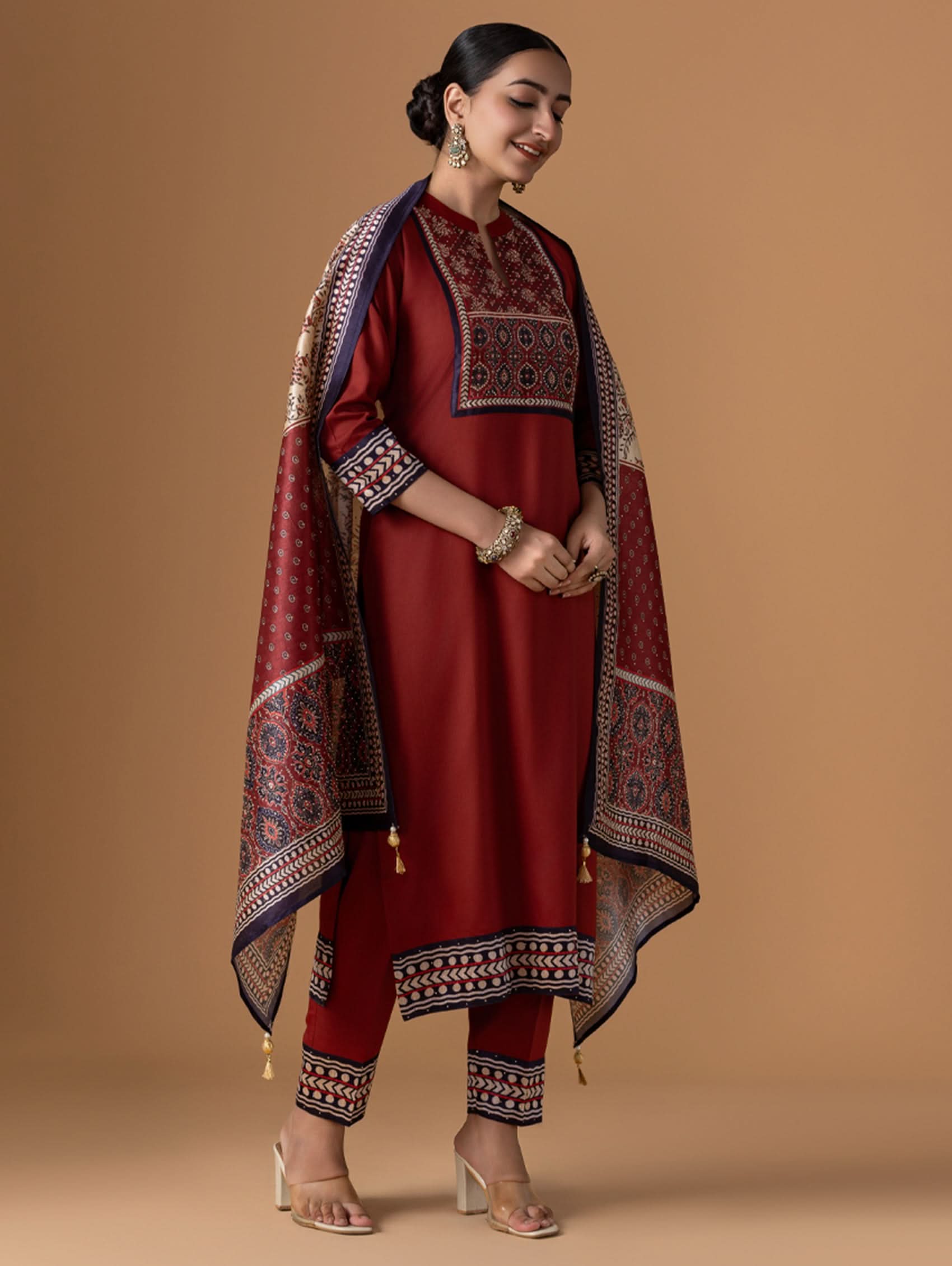 Woman wearing a traditional maroon outfit with a patterned shawl on a beige background