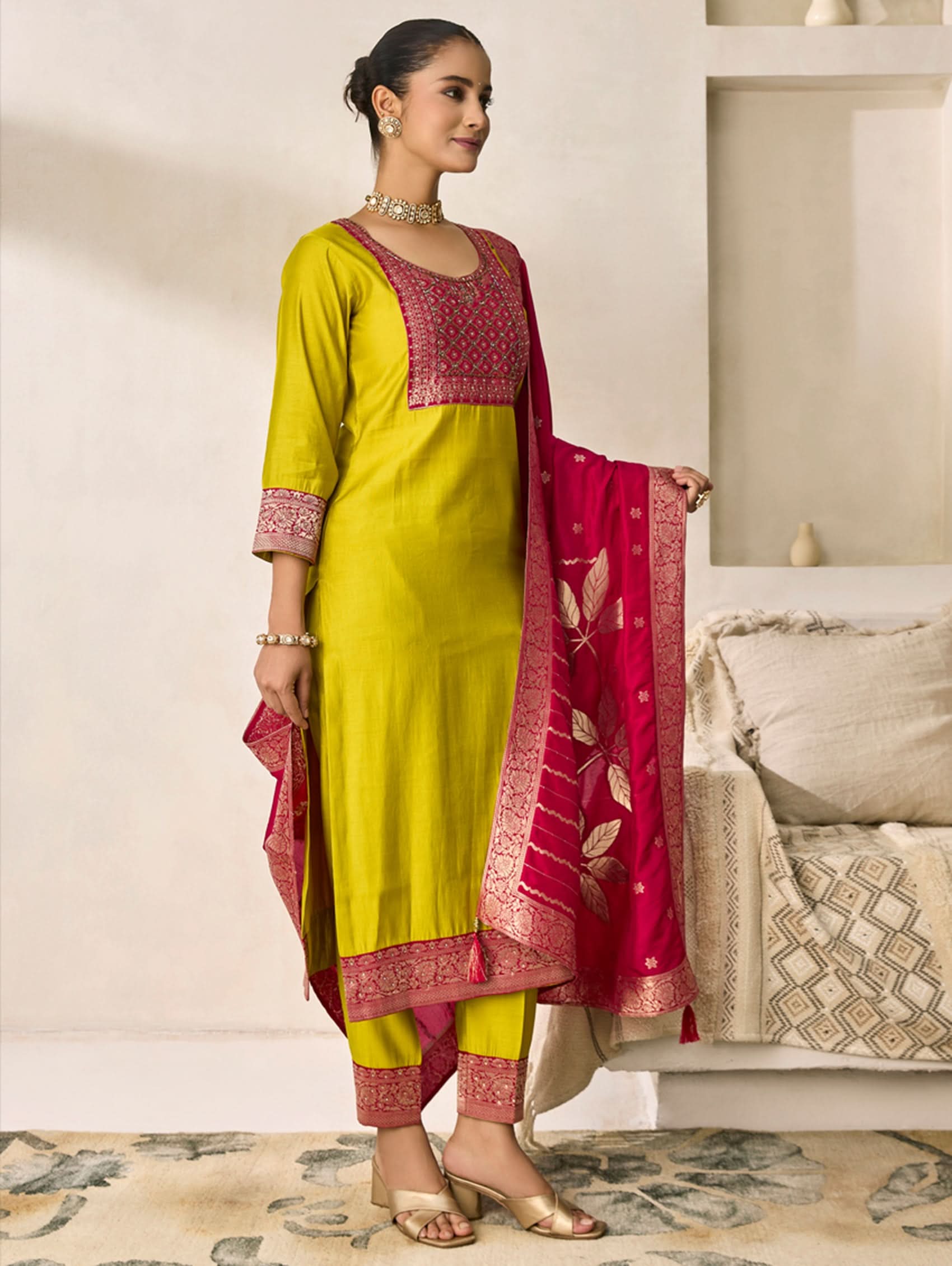 Woman wearing a yellow and pink traditional outfit with a red dupatta in a room.