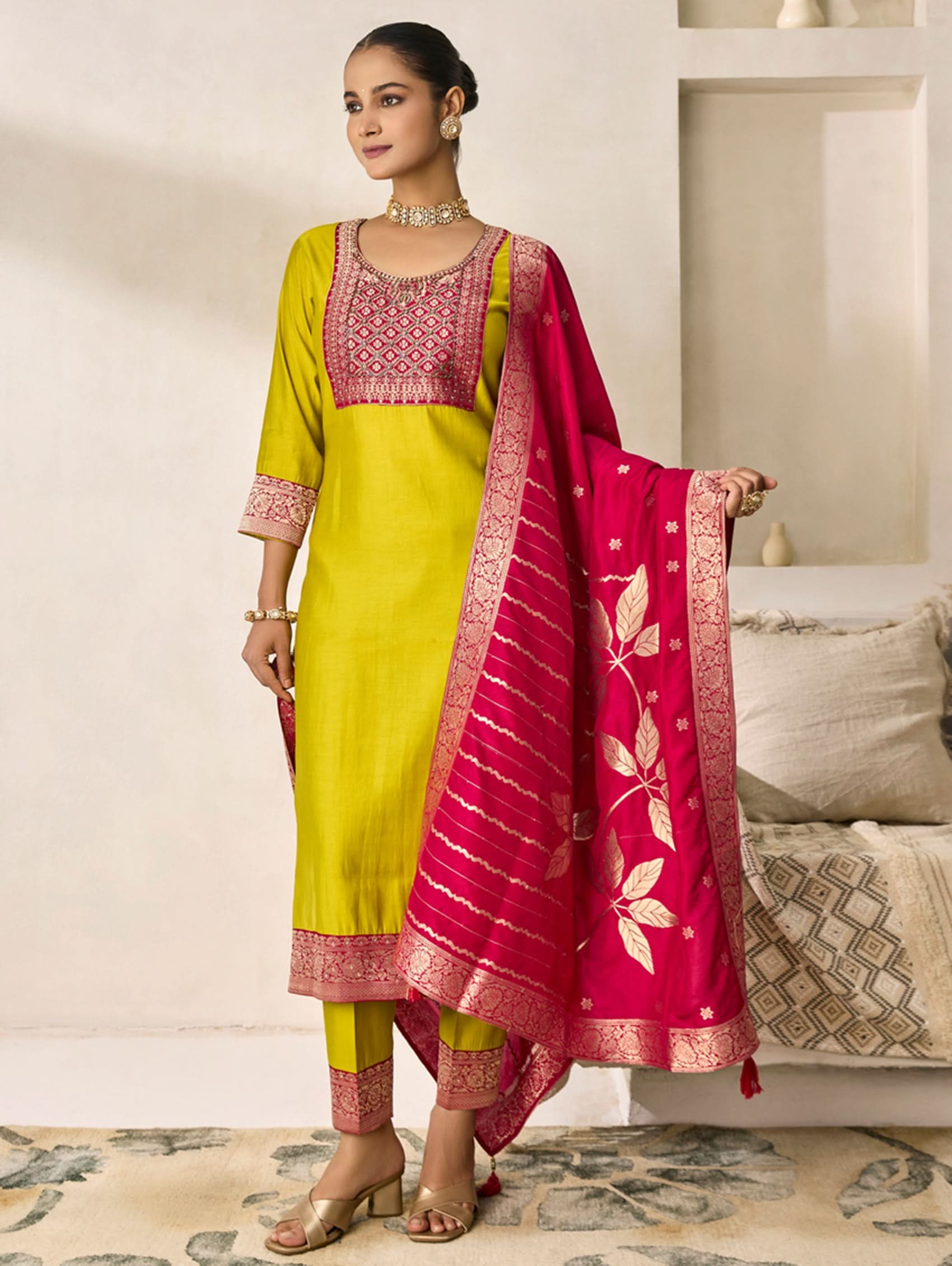 Woman wearing a yellow and pink traditional outfit with a matching dupatta in a living room setting.