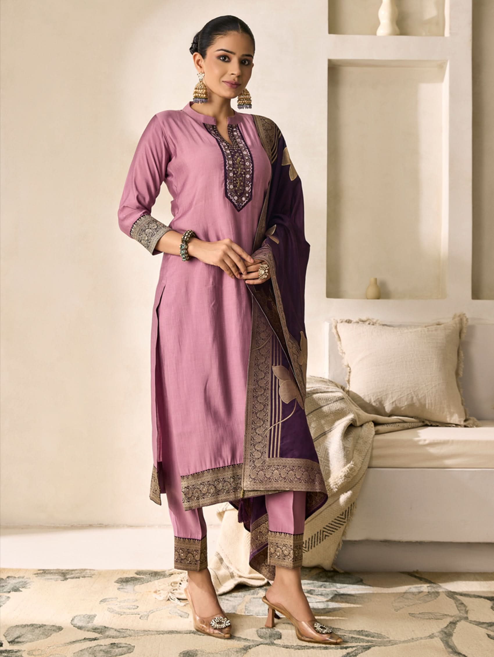 Woman wearing a pink traditional outfit with intricate patterns in a modern living room.