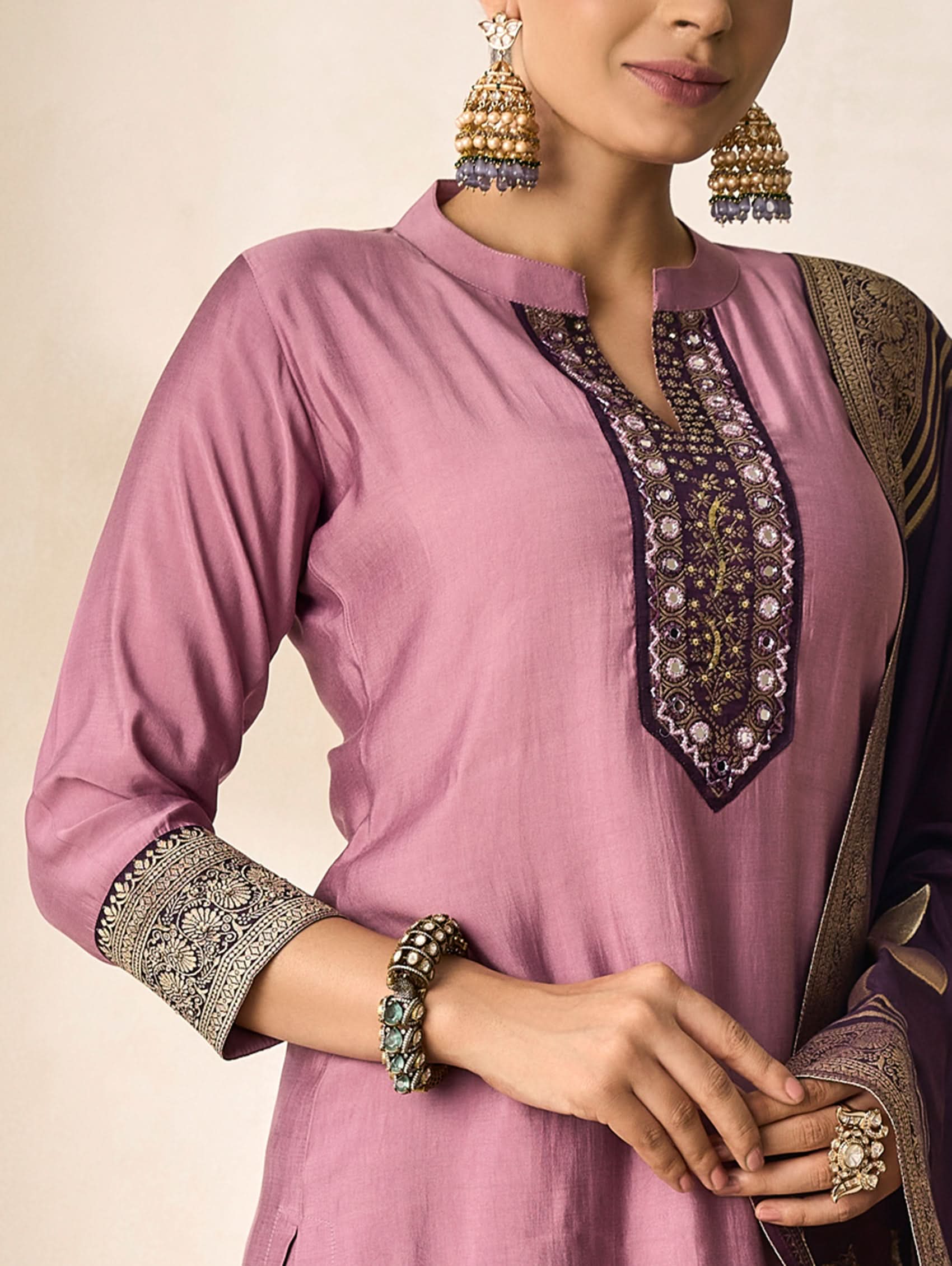 Pink traditional outfit with intricate embroidery and jewelry on a neutral background