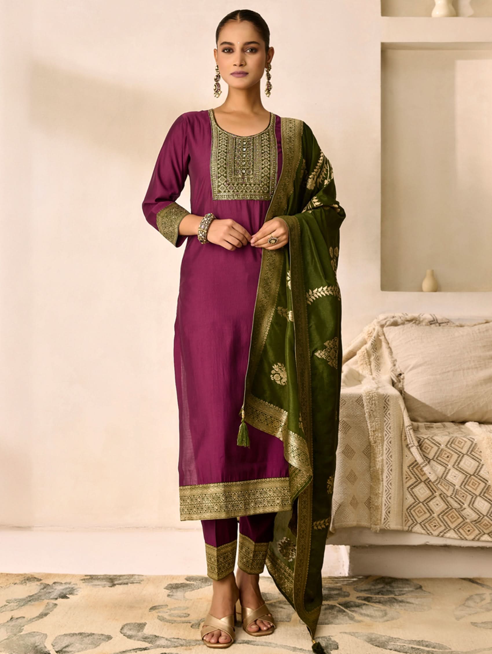 Woman wearing a purple and green traditional outfit in a room with a beige sofa.