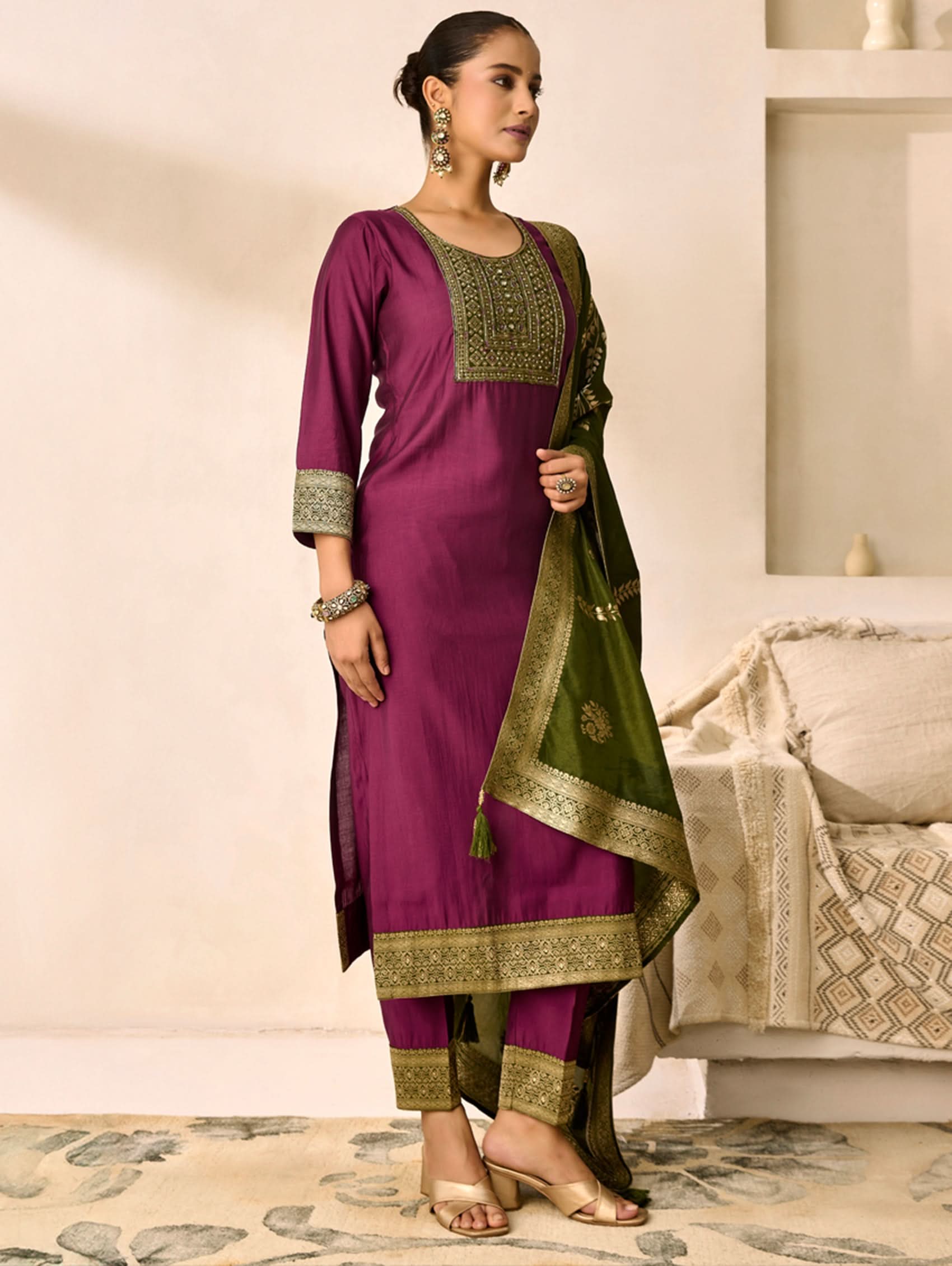 Woman wearing a purple and green traditional outfit in a room with a white sofa.