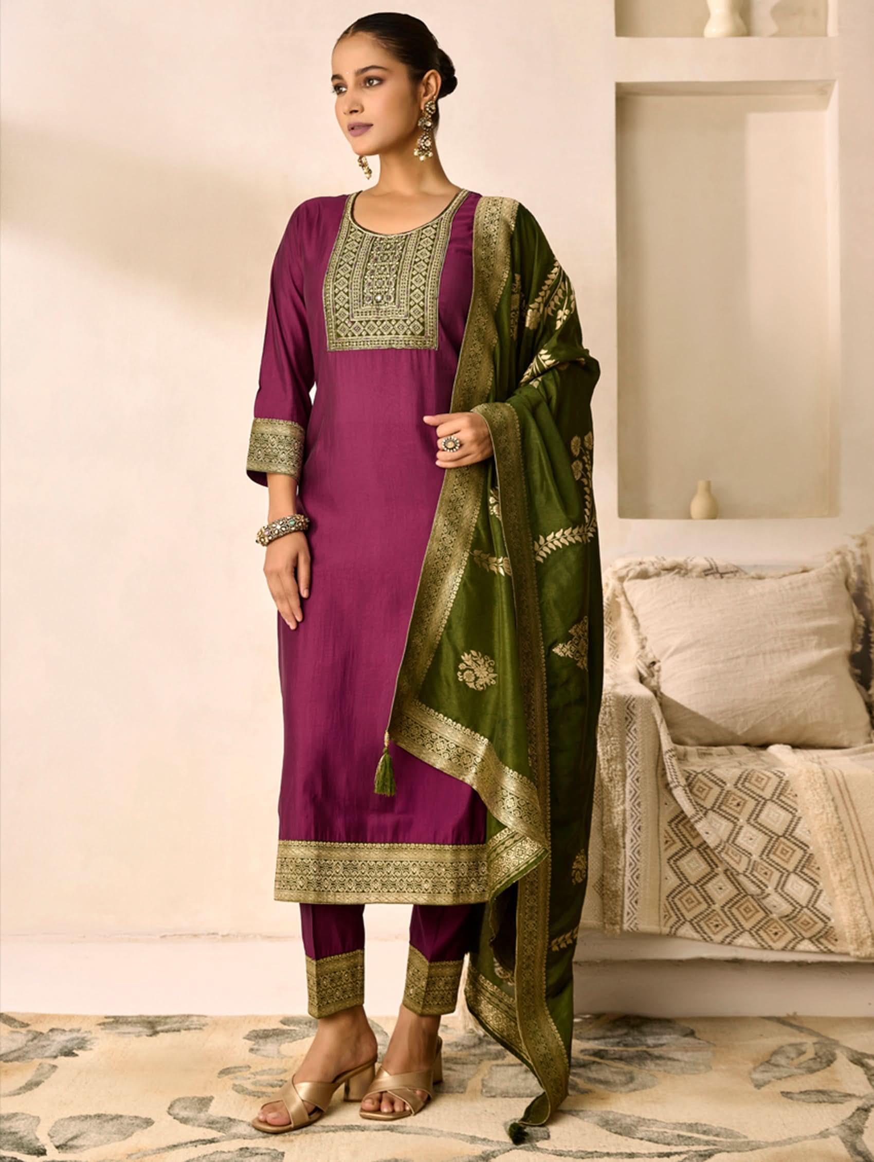 Woman wearing a purple and green traditional outfit with a matching dupatta in a room.