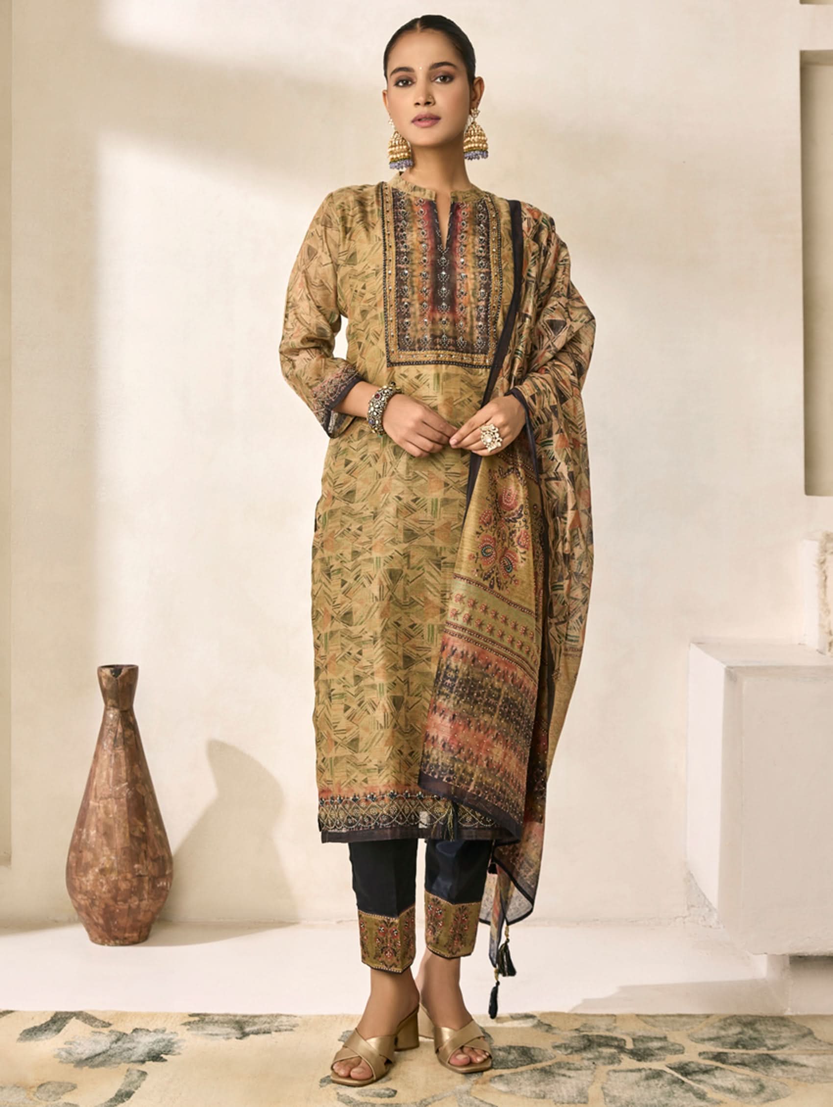 Woman wearing a traditional outfit with a patterned dupatta in a minimalistic room.
