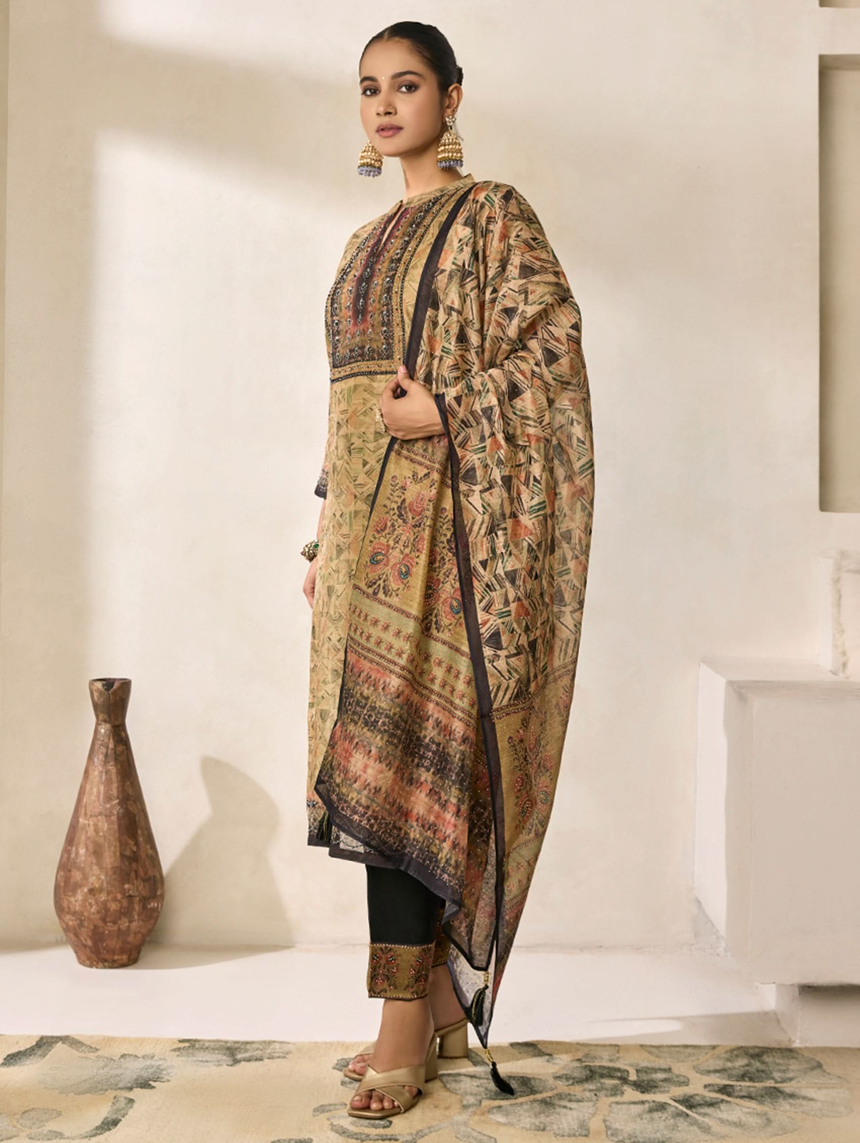 Woman wearing a traditional outfit with a patterned dupatta in a minimalistic setting.