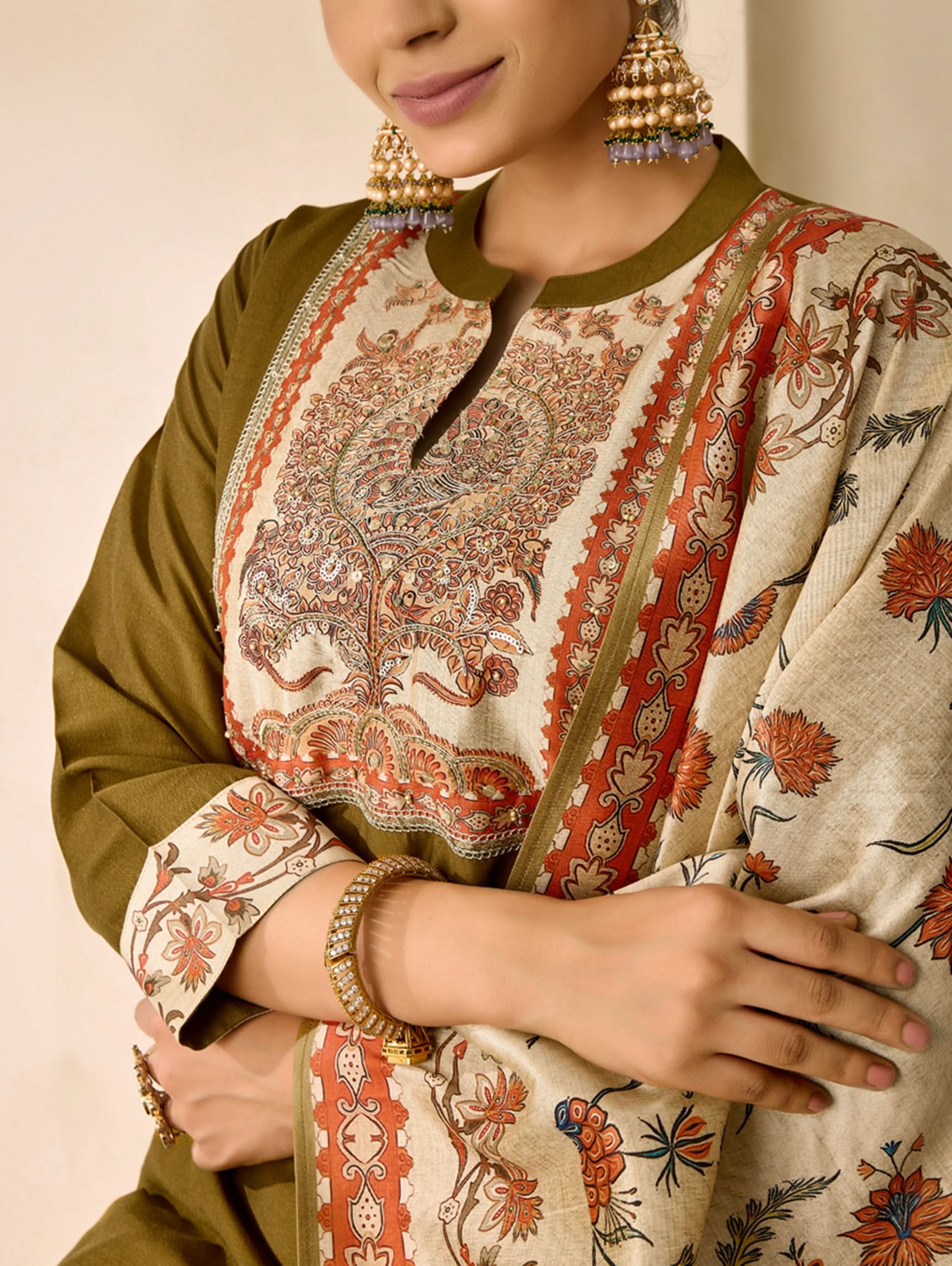 Woman wearing a traditional outfit with floral patterns and gold jewelry against a neutral background