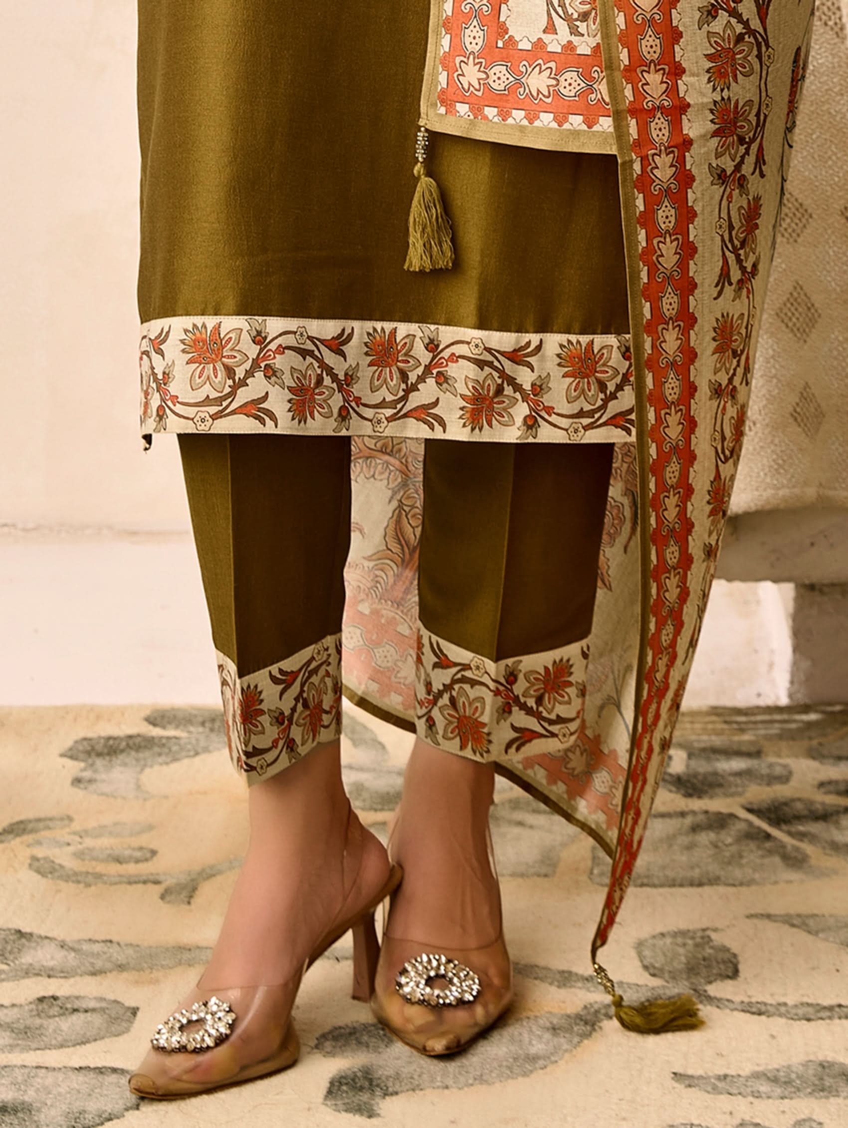 Traditional outfit with embroidered green kurta, pants, and dupatta on a patterned floor.