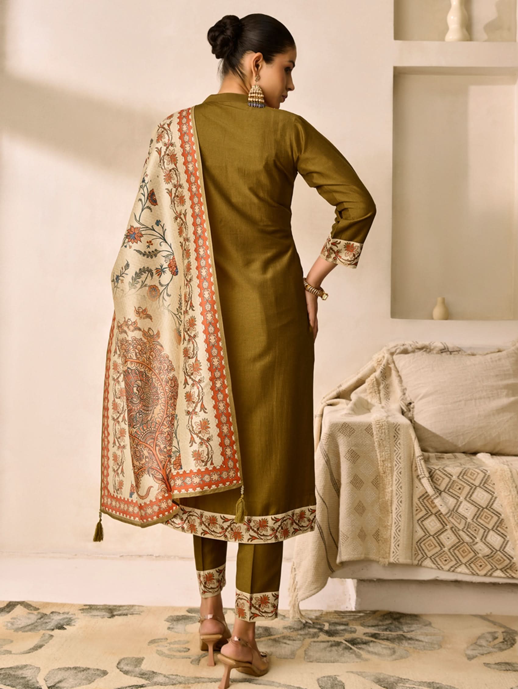 Woman in a green traditional outfit with a patterned scarf in a room.