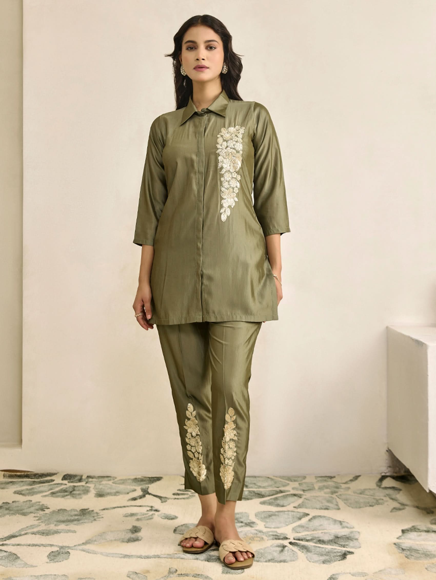 Woman wearing a green outfit with floral embroidery in a minimal indoor setting