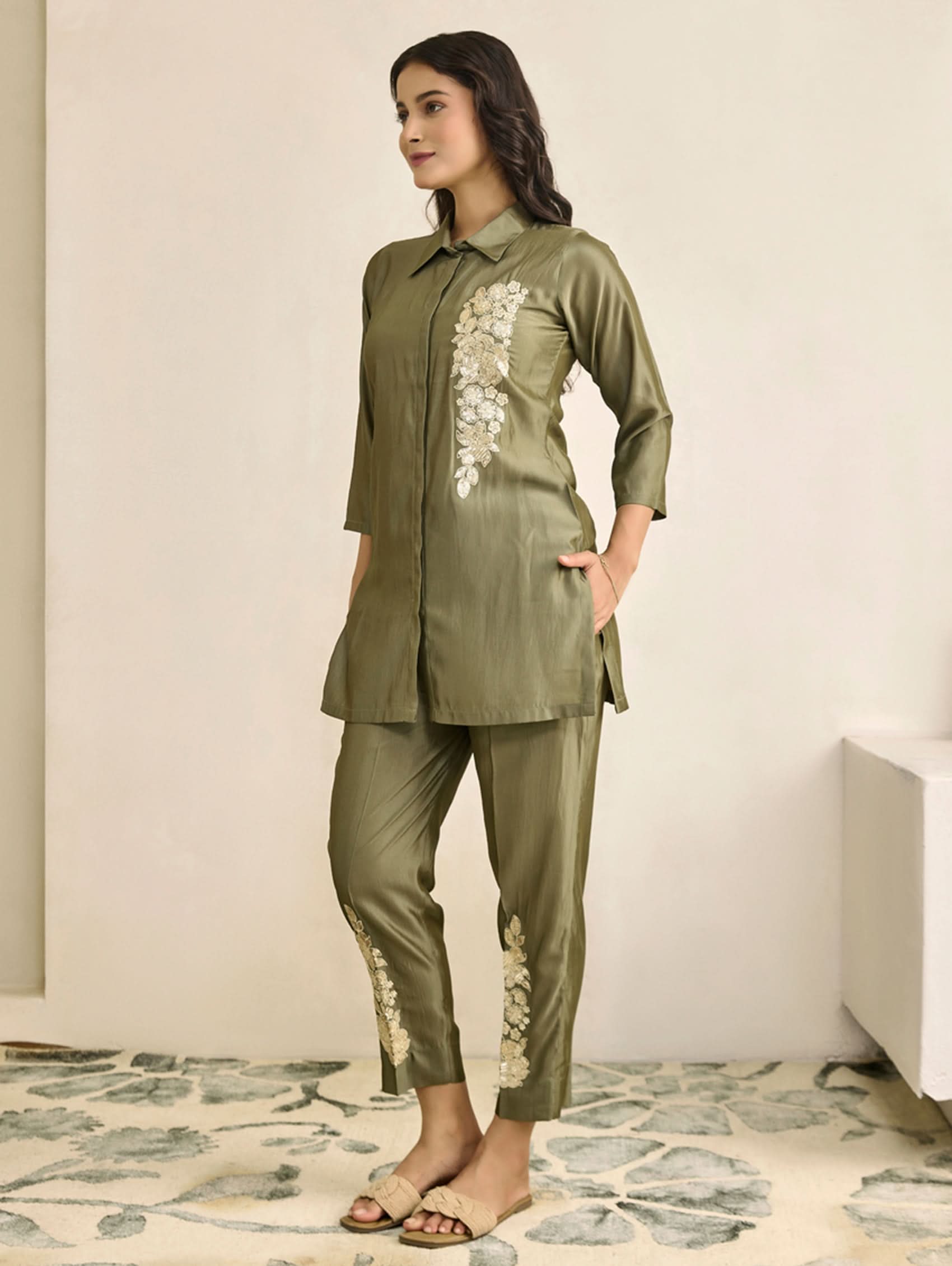 Woman wearing a green outfit with floral embroidery on a neutral background