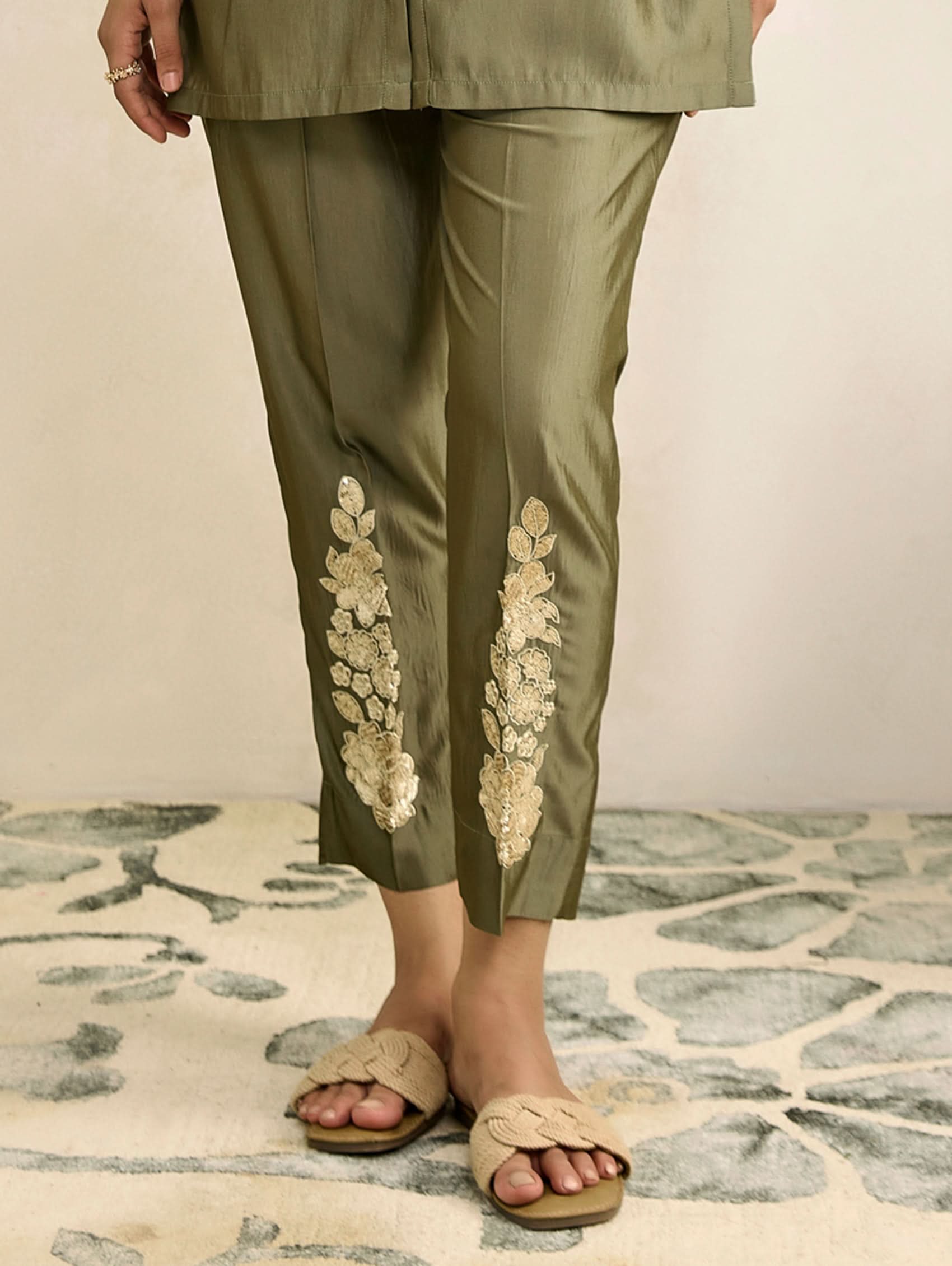 Green pants with floral embroidery worn by a person on a stone floor.
