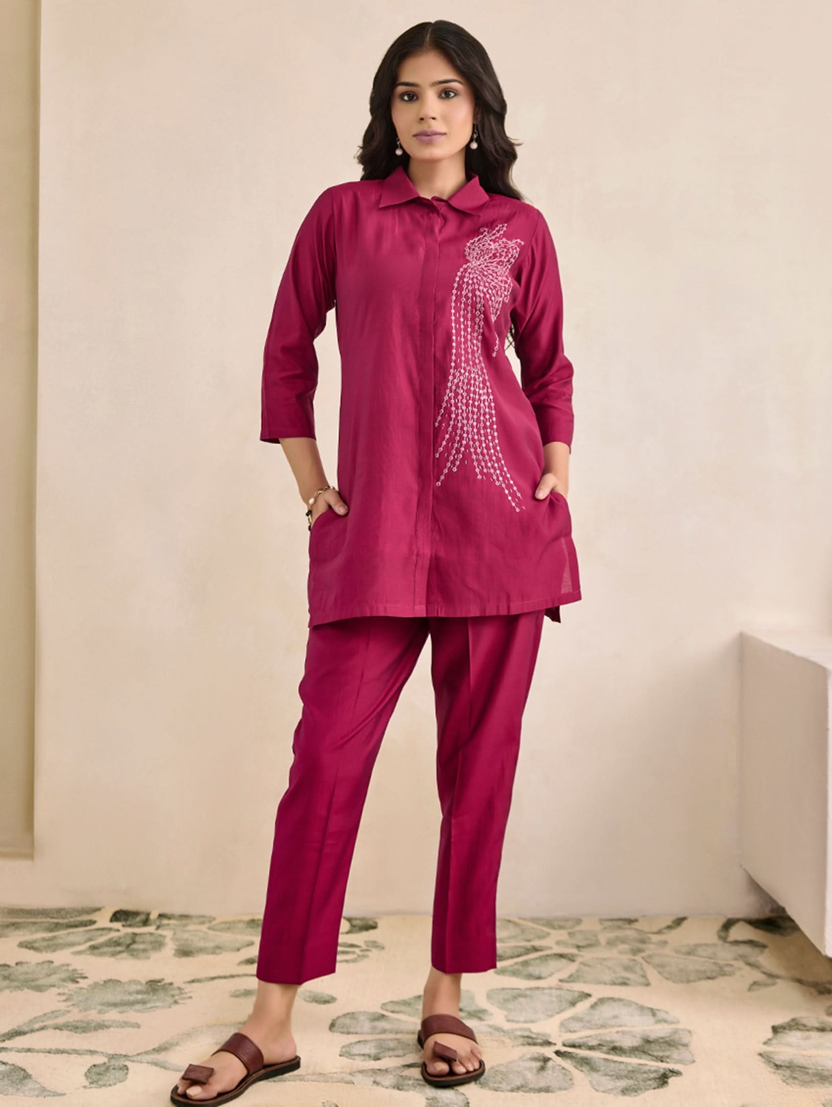 Woman wearing a magenta traditional outfit with a peacock design on a neutral background