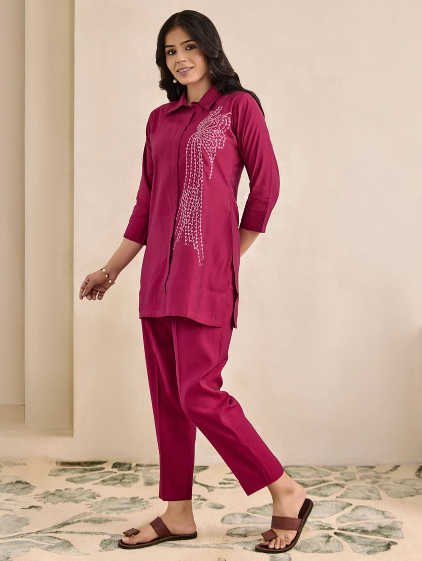 Woman wearing a magenta outfit with intricate detailing on a neutral background