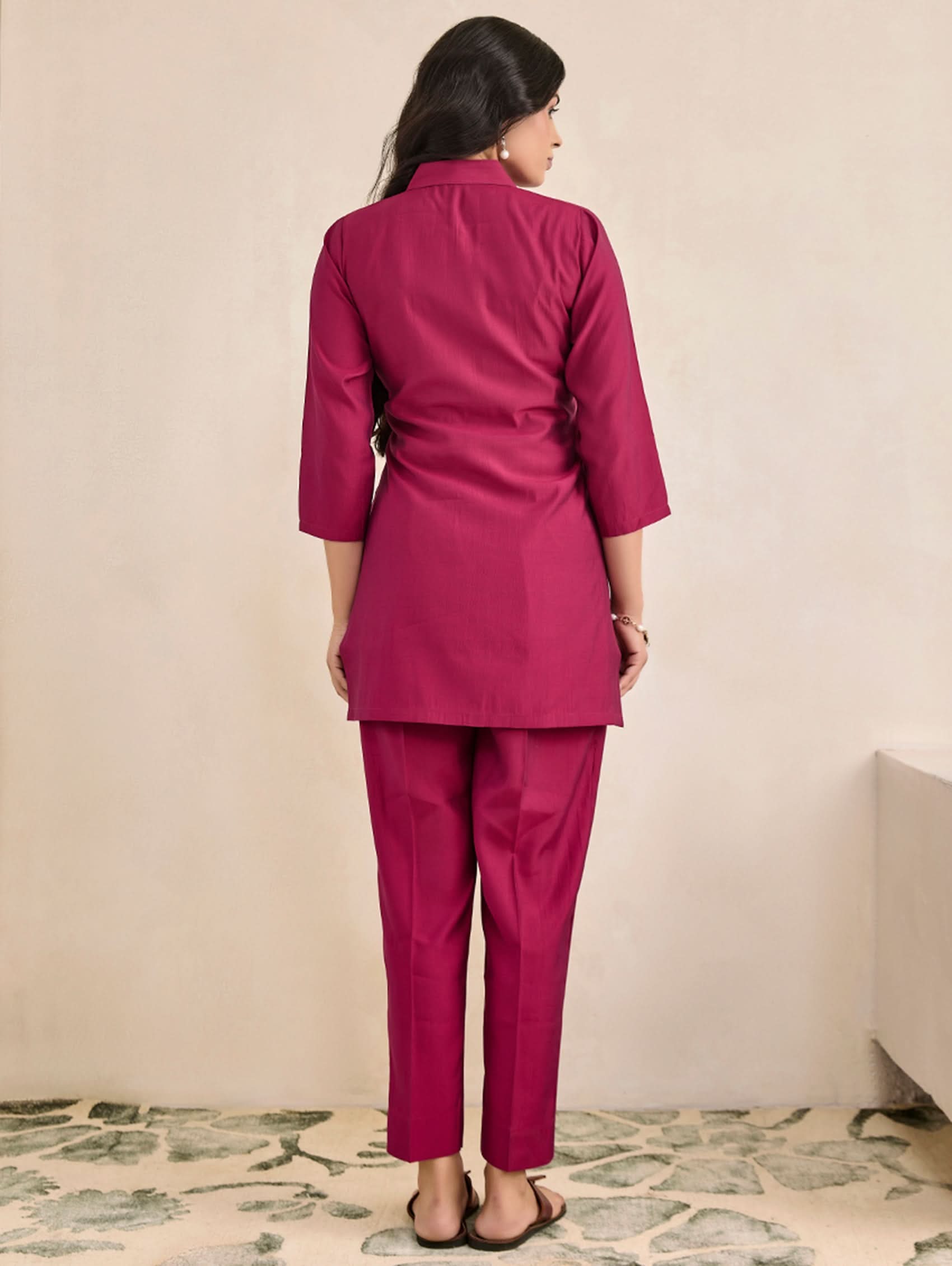 Woman wearing a magenta suit standing against a beige wall.