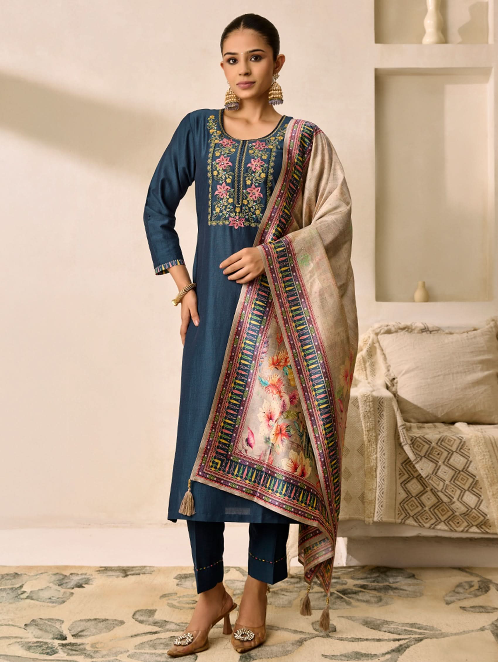Woman wearing a blue embroidered kurta with a beige dupatta in a decorated room.