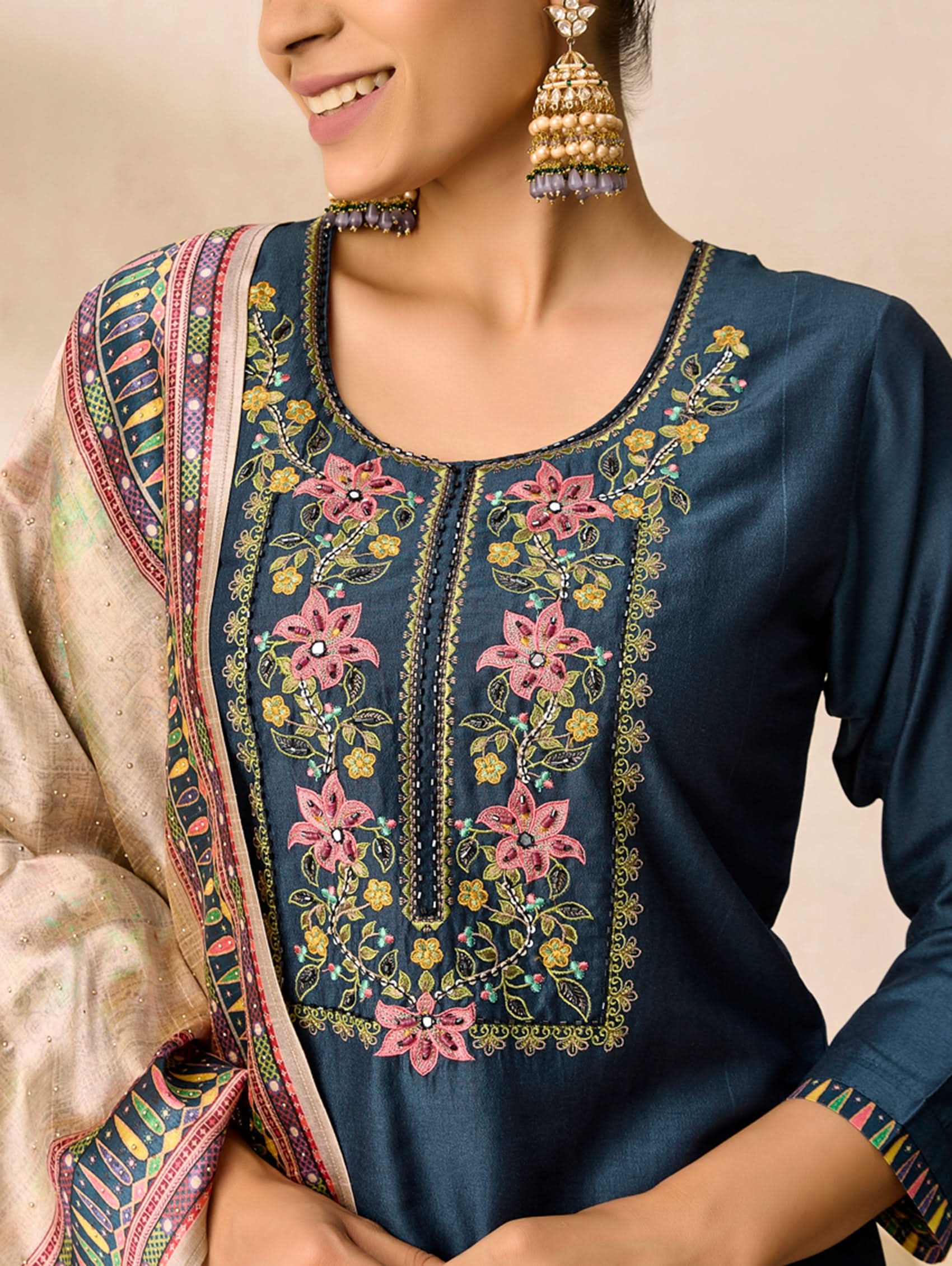 Woman wearing a navy blue embroidered top with colorful floral patterns on a beige background