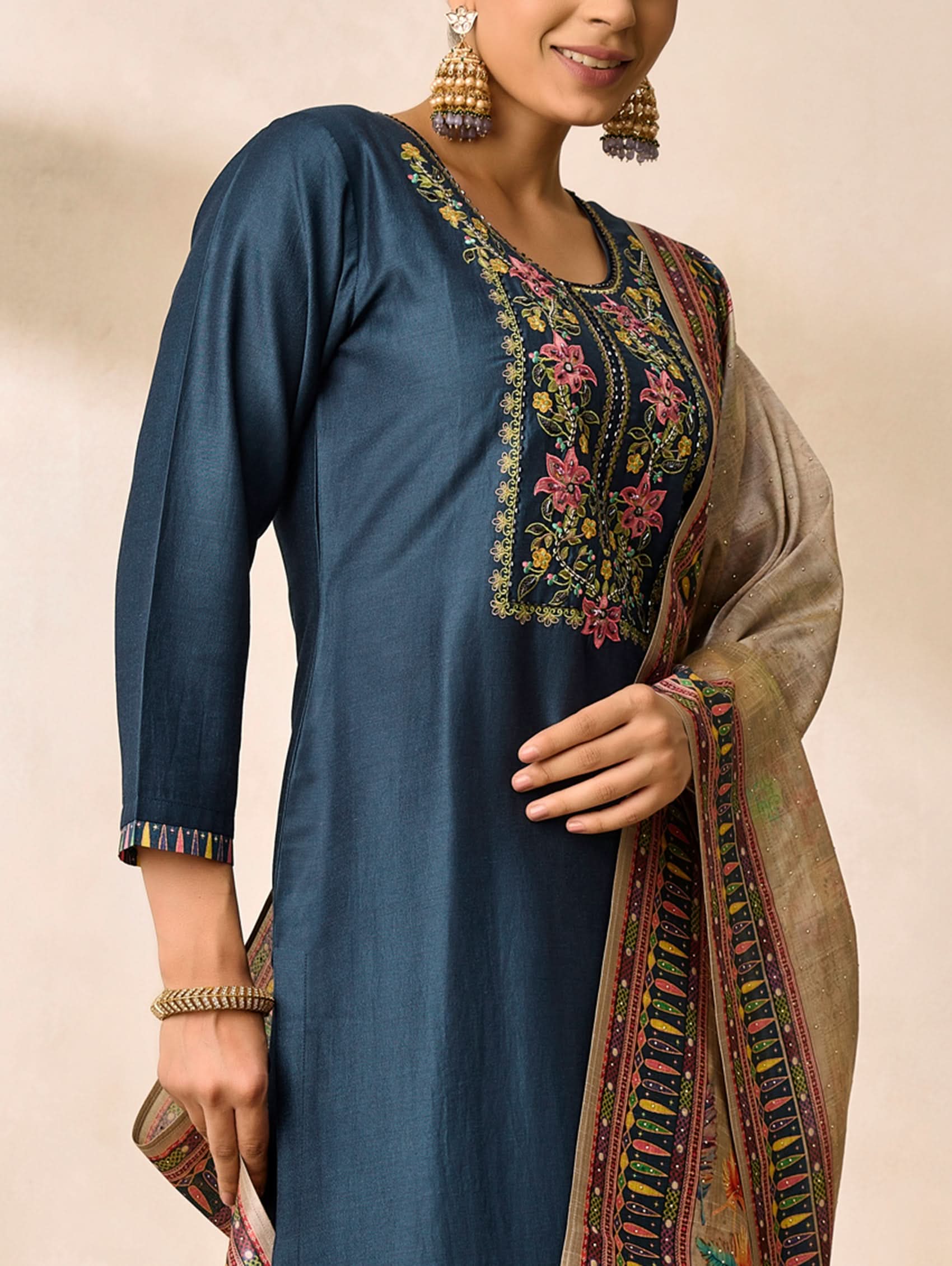 Woman wearing a blue embroidered kurta with a matching shawl on a beige background
