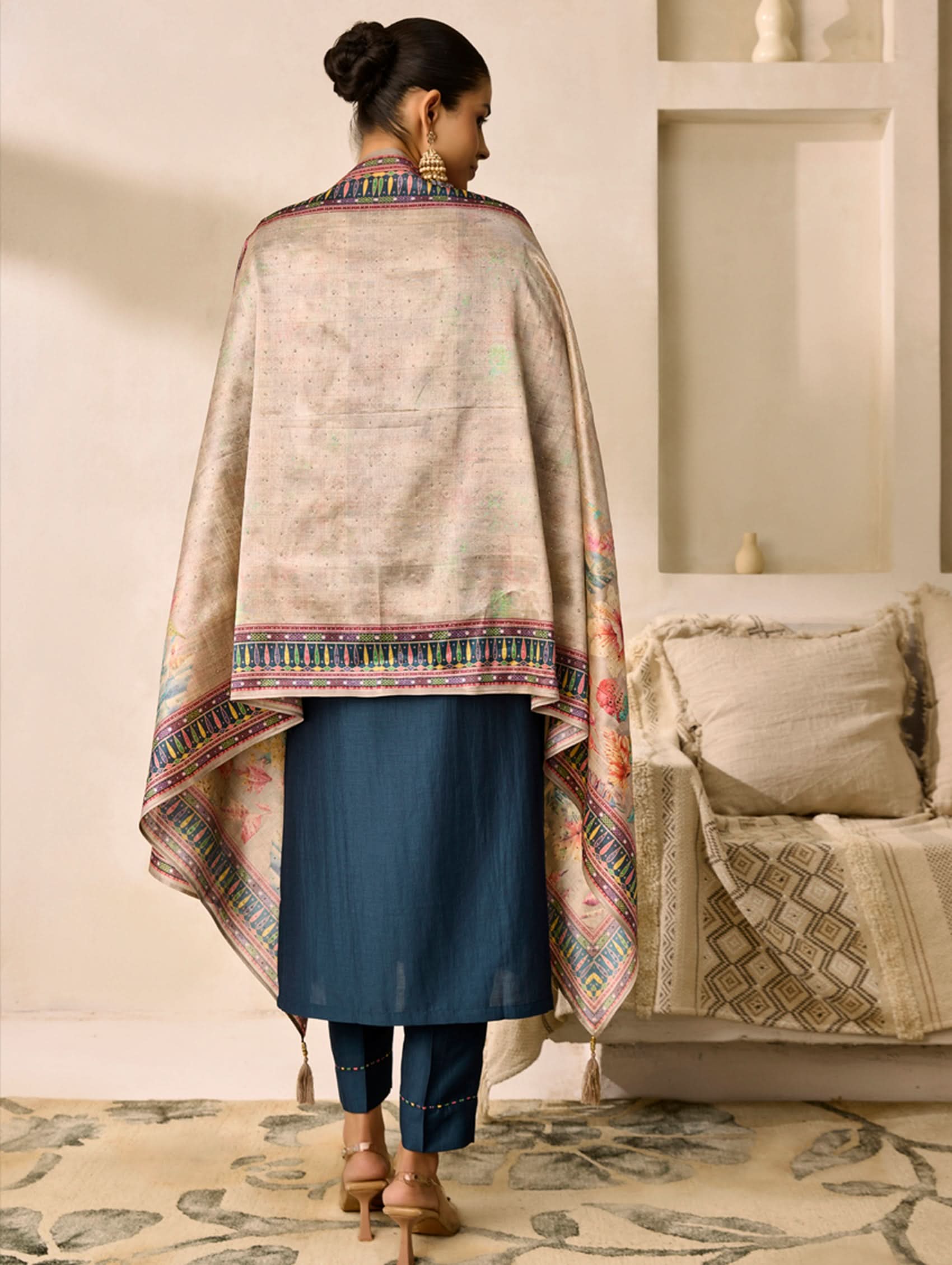 Woman wearing a traditional outfit with a patterned shawl in a living room setting.