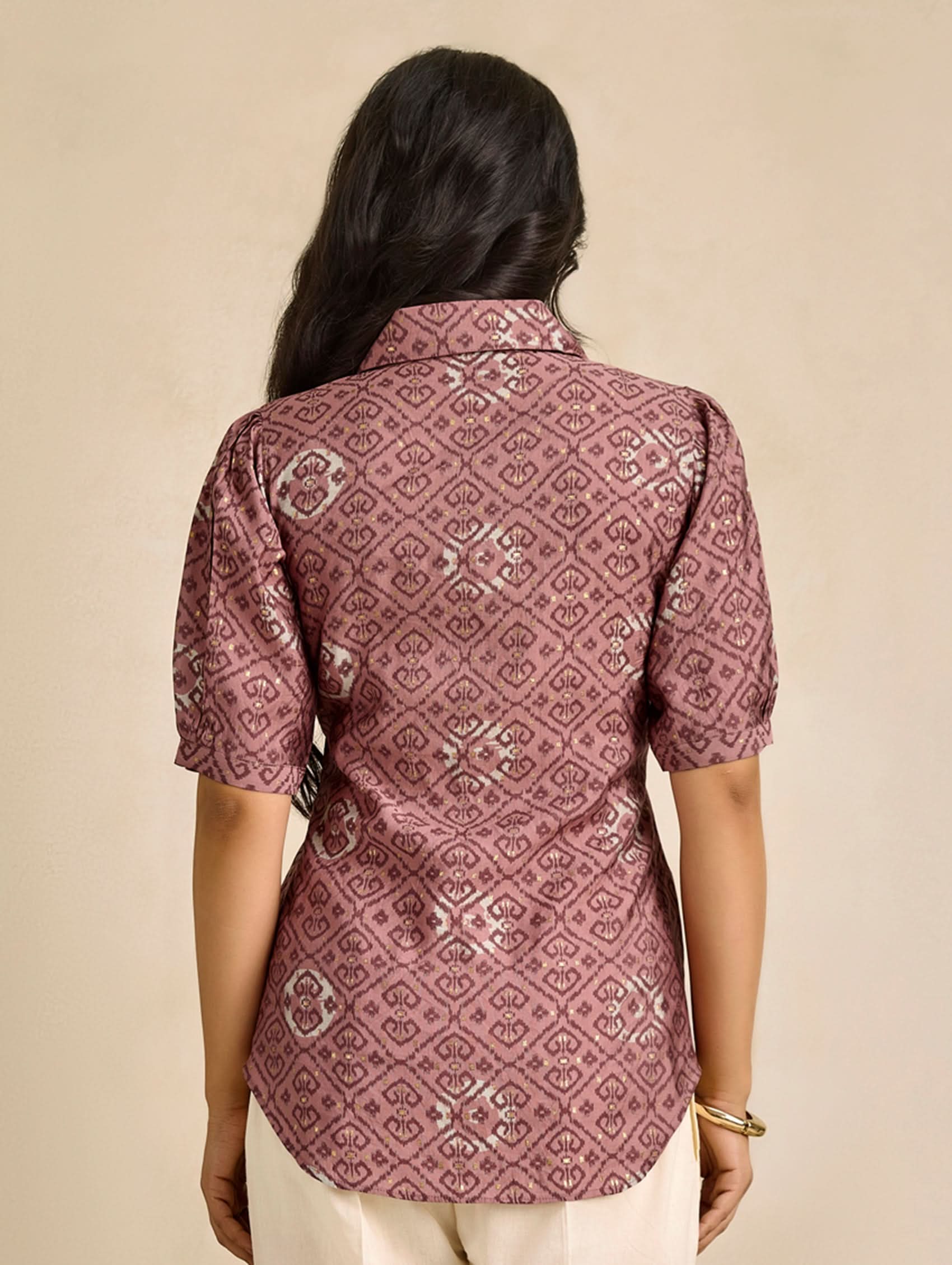 Person wearing a patterned maroon shirt on a beige background