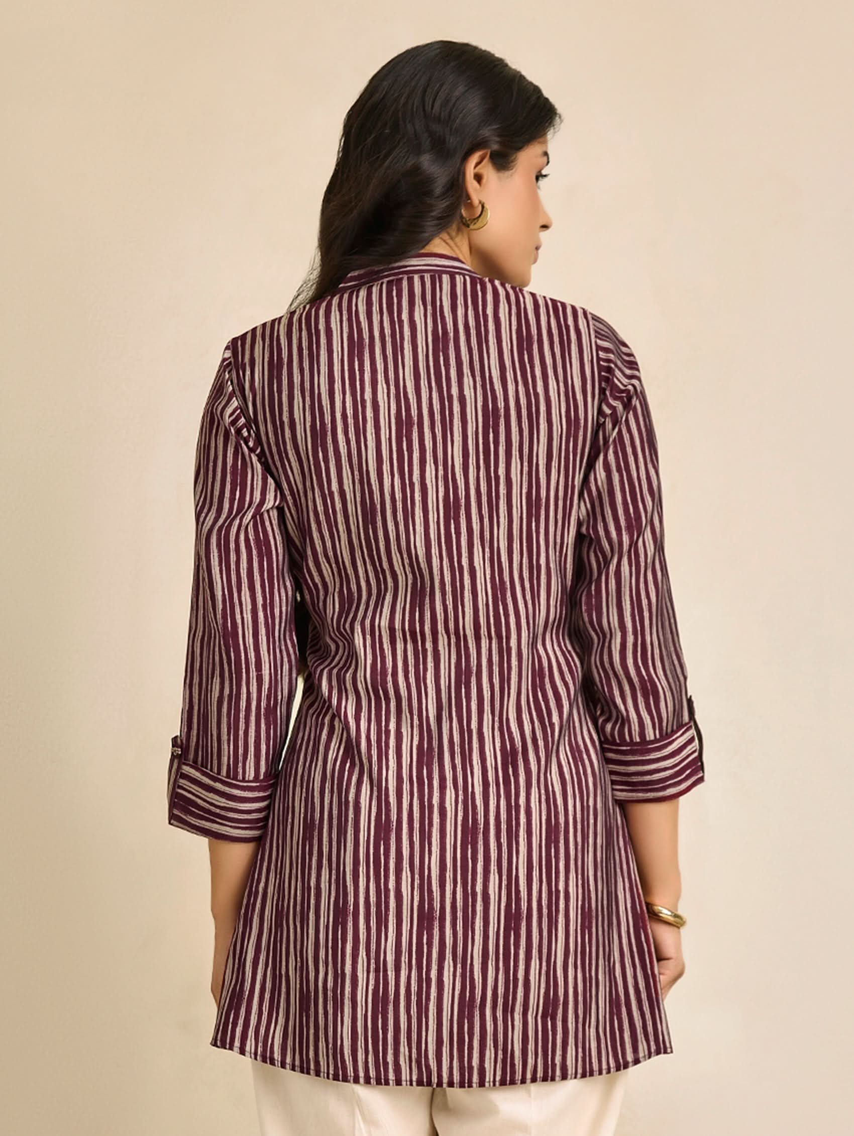 Woman wearing a maroon and white striped kurta against a beige background