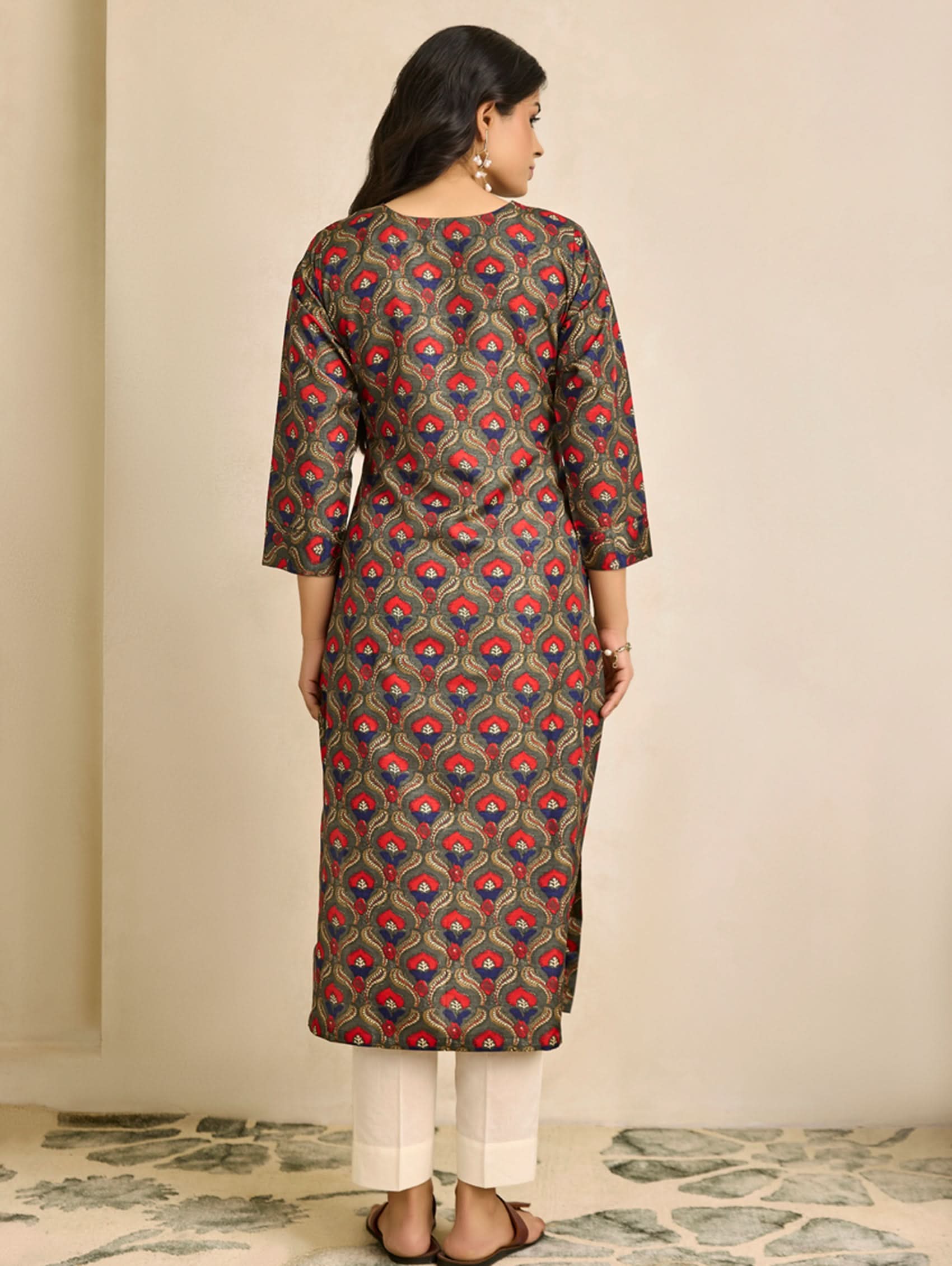 Woman wearing a patterned kurta with white pants against a beige wall.