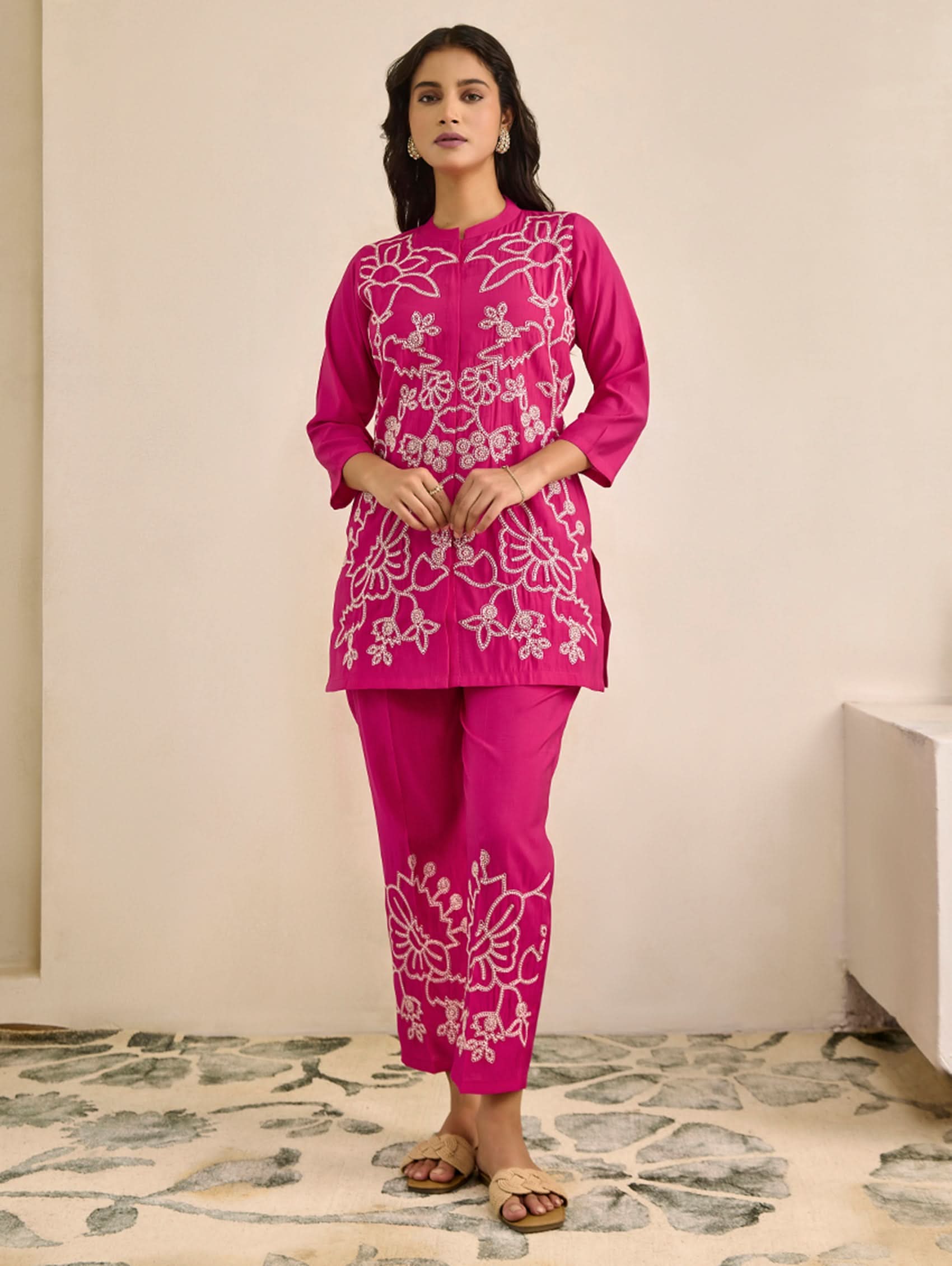 Woman wearing a pink embroidered outfit standing in a room with a neutral background