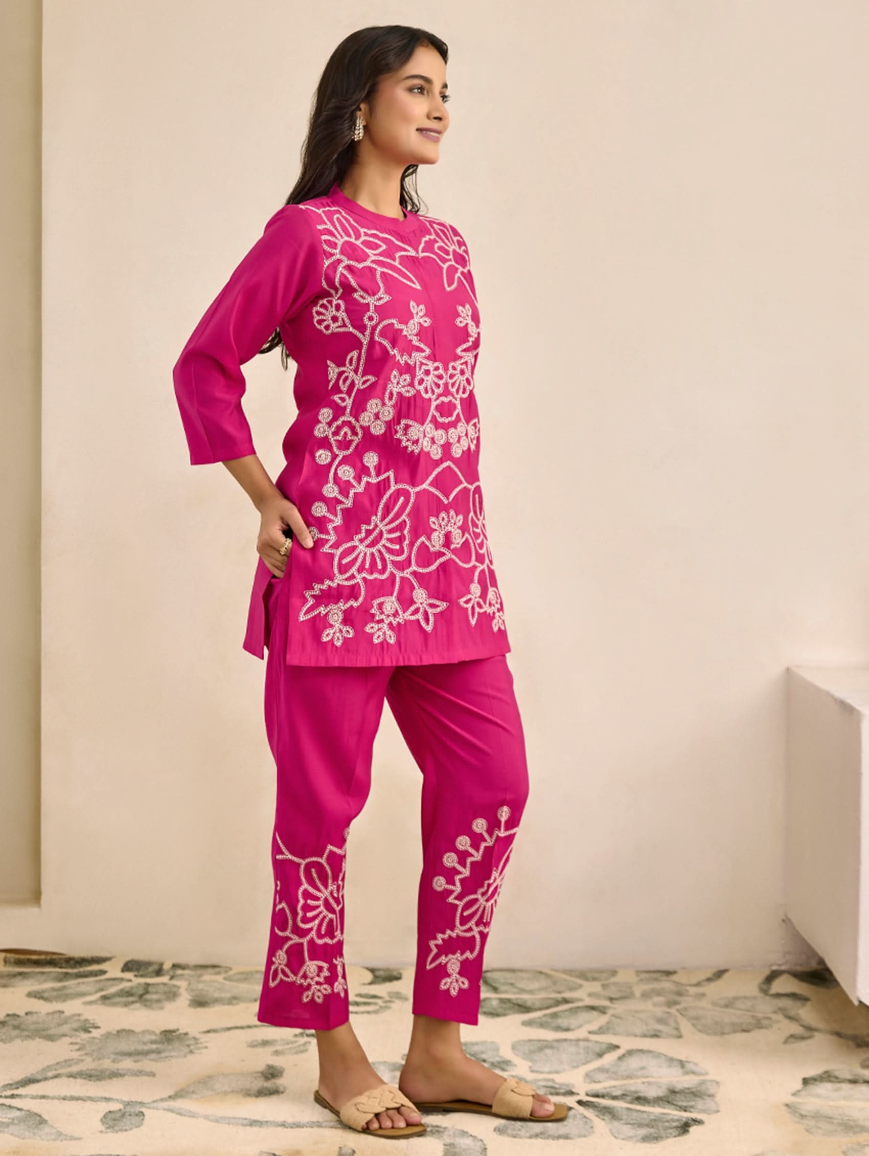 Woman wearing a pink embroidered outfit in a minimal indoor setting