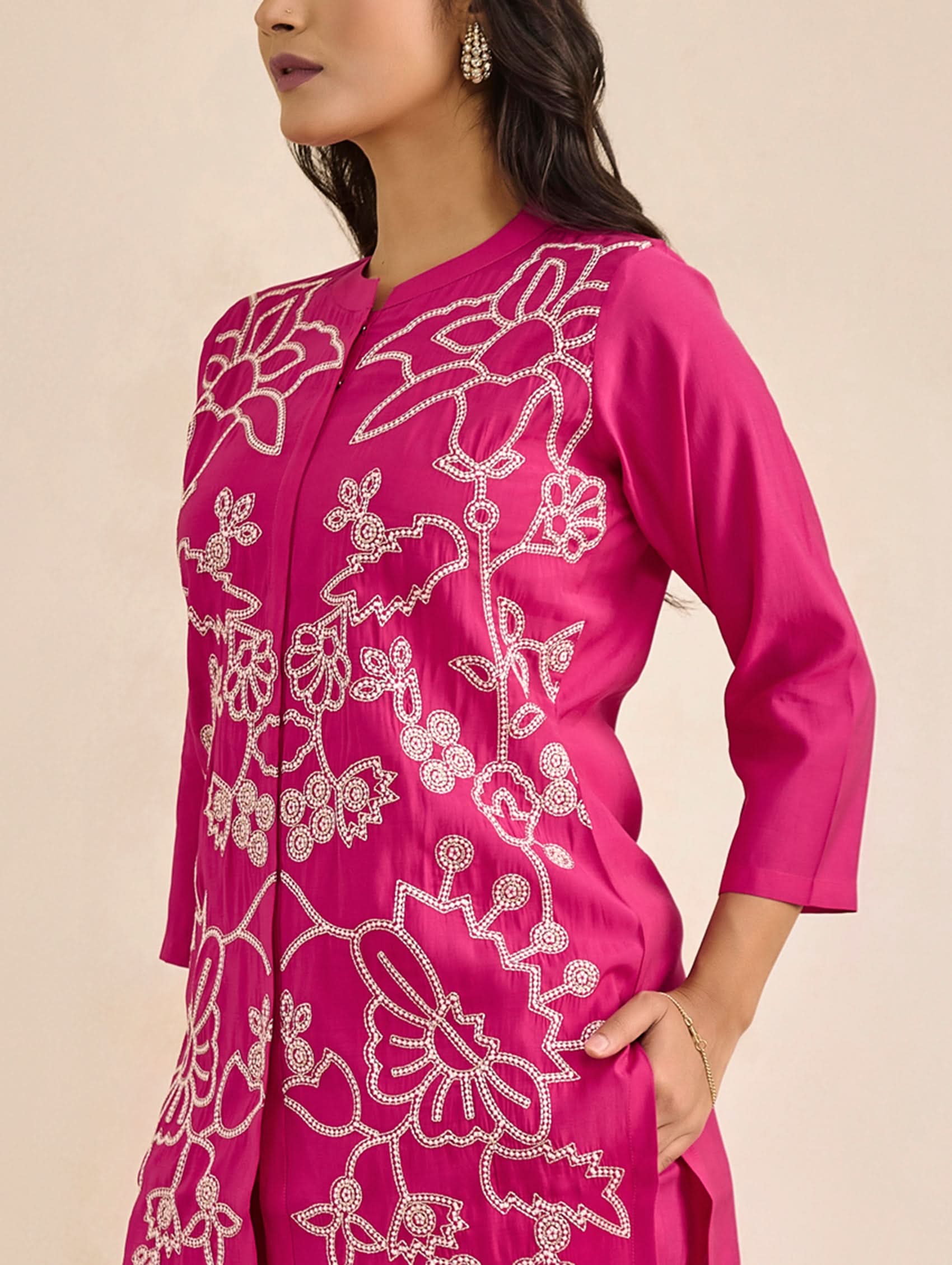 Woman wearing a pink embroidered outfit with a neutral background