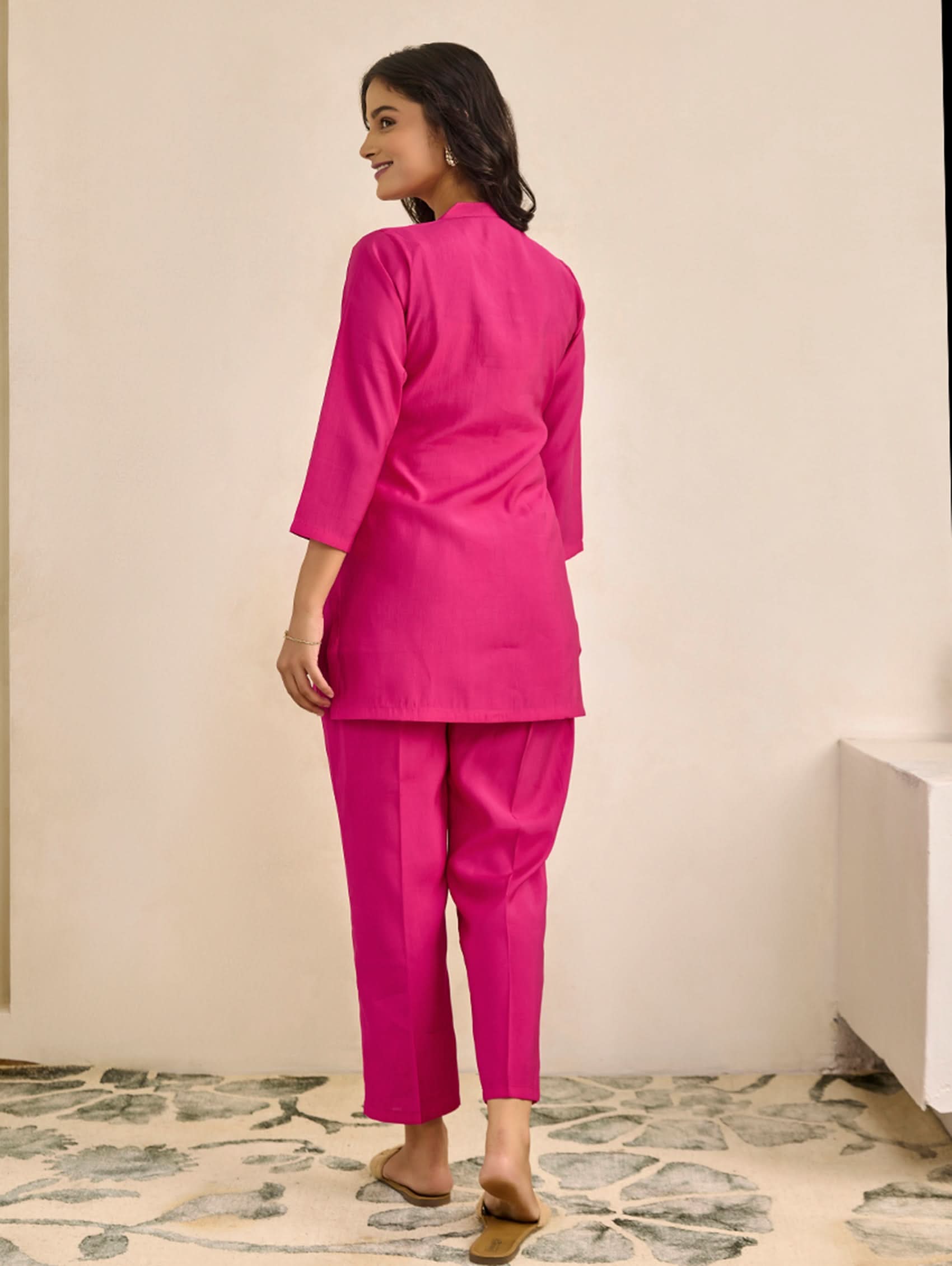 Woman wearing a bright pink outfit standing in a room with a stone floor.