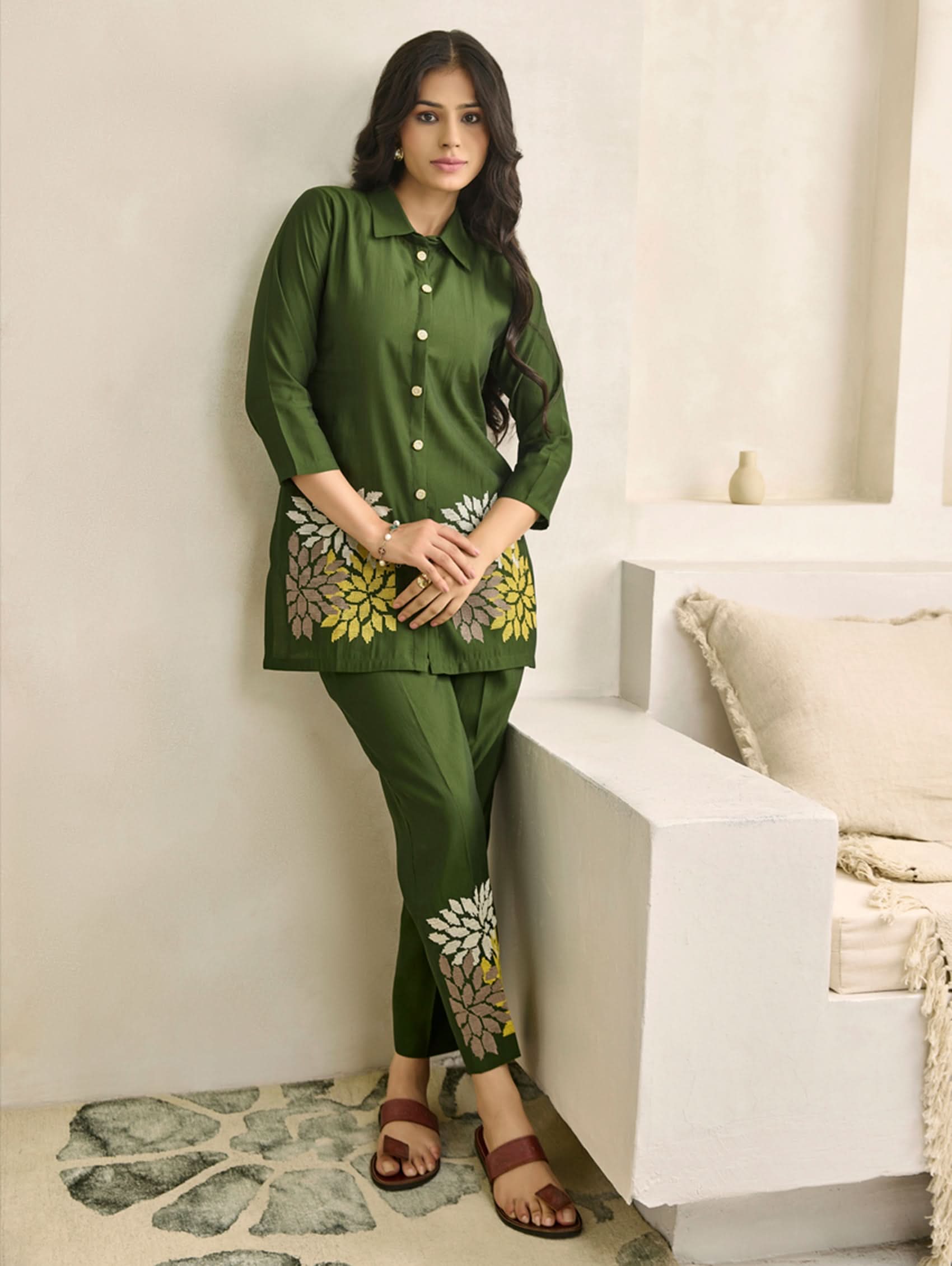 Woman wearing a green traditional outfit with floral patterns in a minimalistic room.