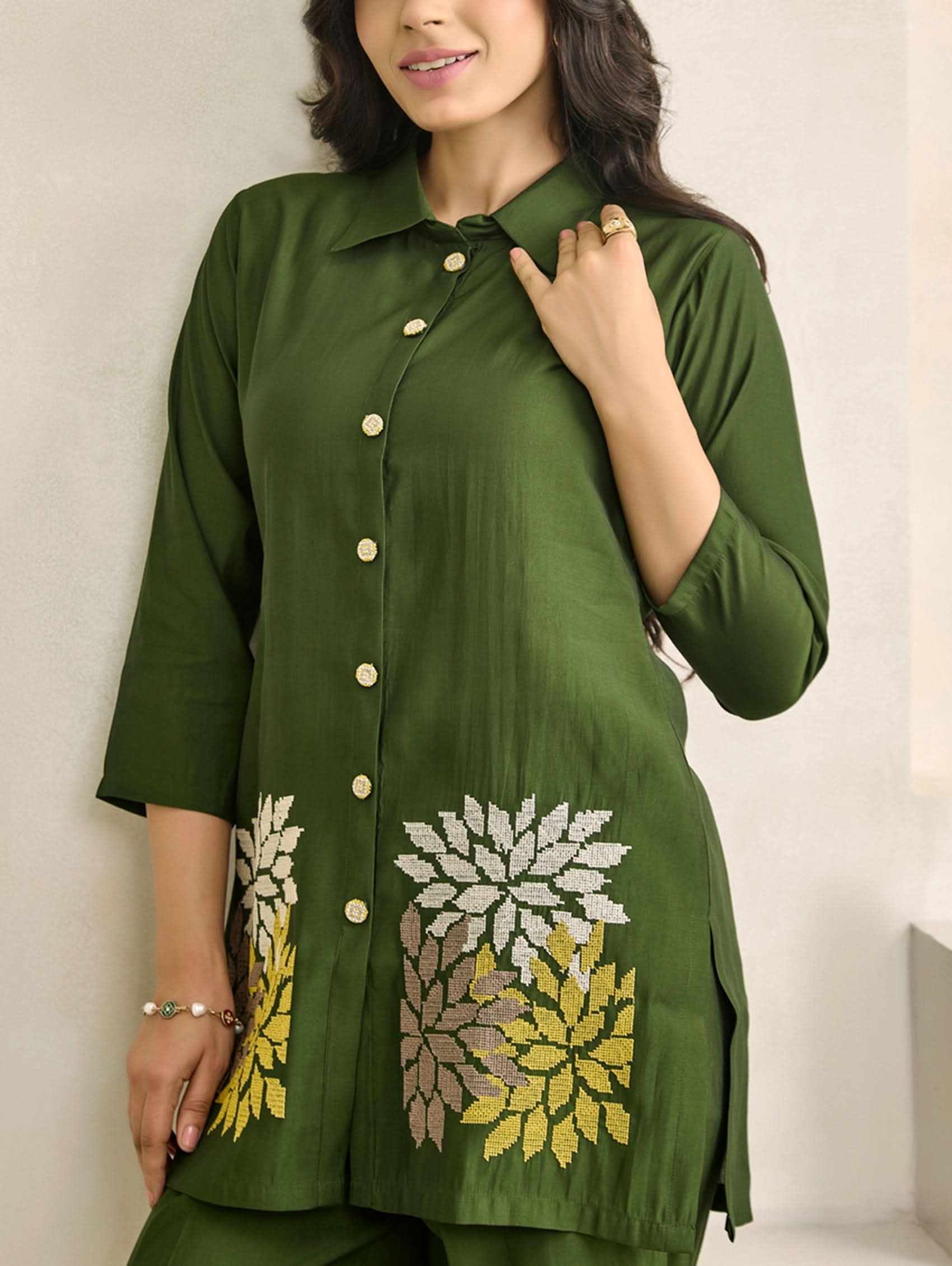 Woman wearing a green outfit with floral embroidery on a plain background