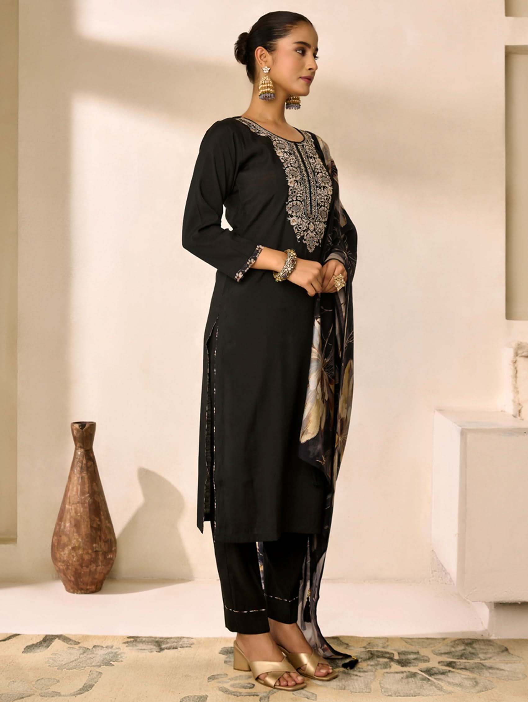 Woman wearing a black traditional outfit with intricate designs in a minimalistic setting.