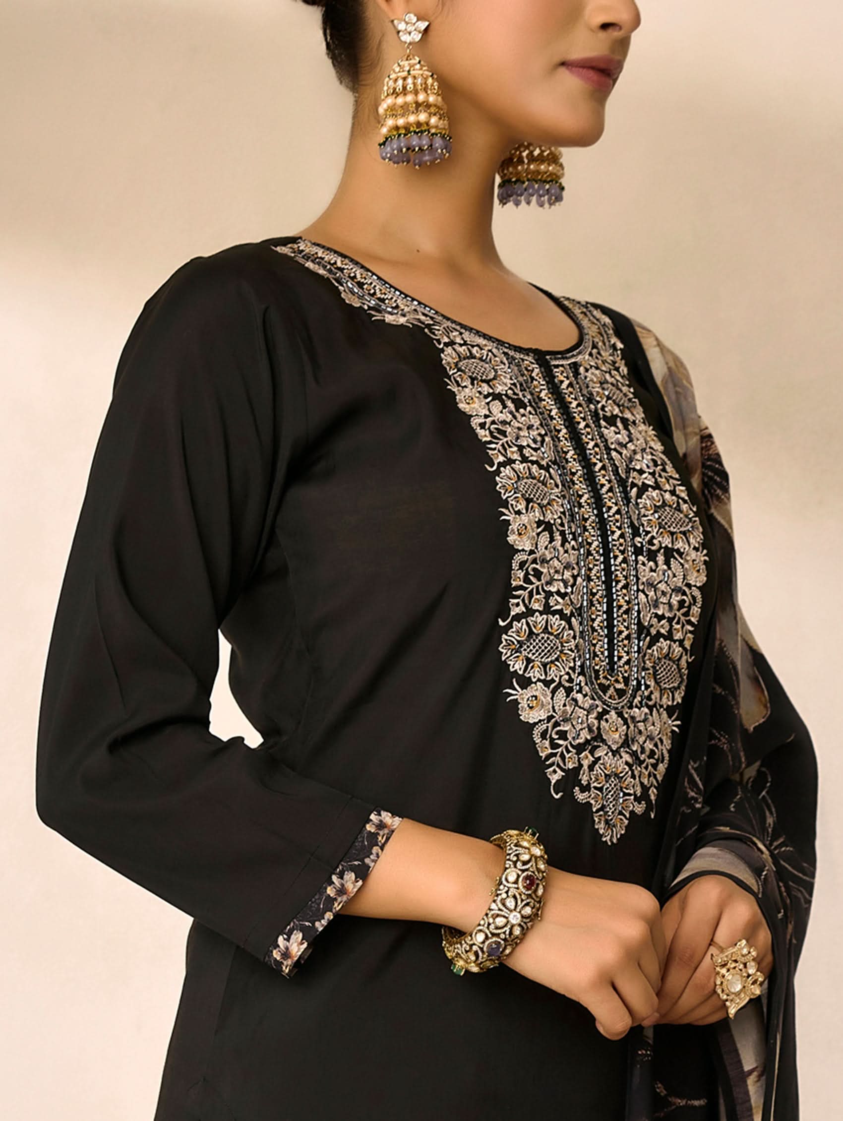 Black outfit with intricate silver embroidery on a beige background
