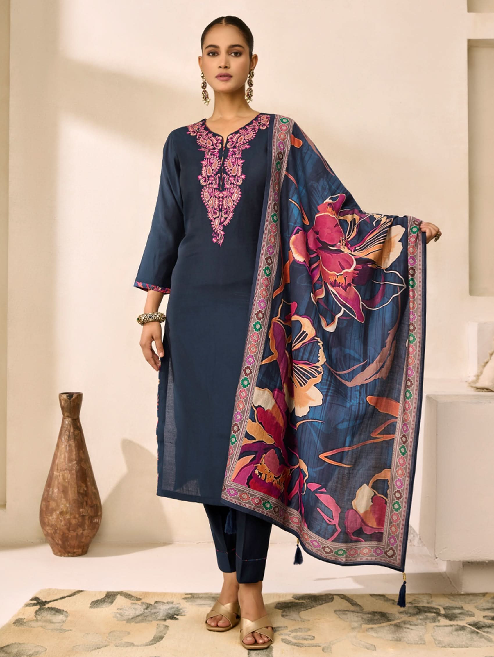 Woman wearing a navy blue kurta with pink embroidery and a floral dupatta in a minimalistic setting.