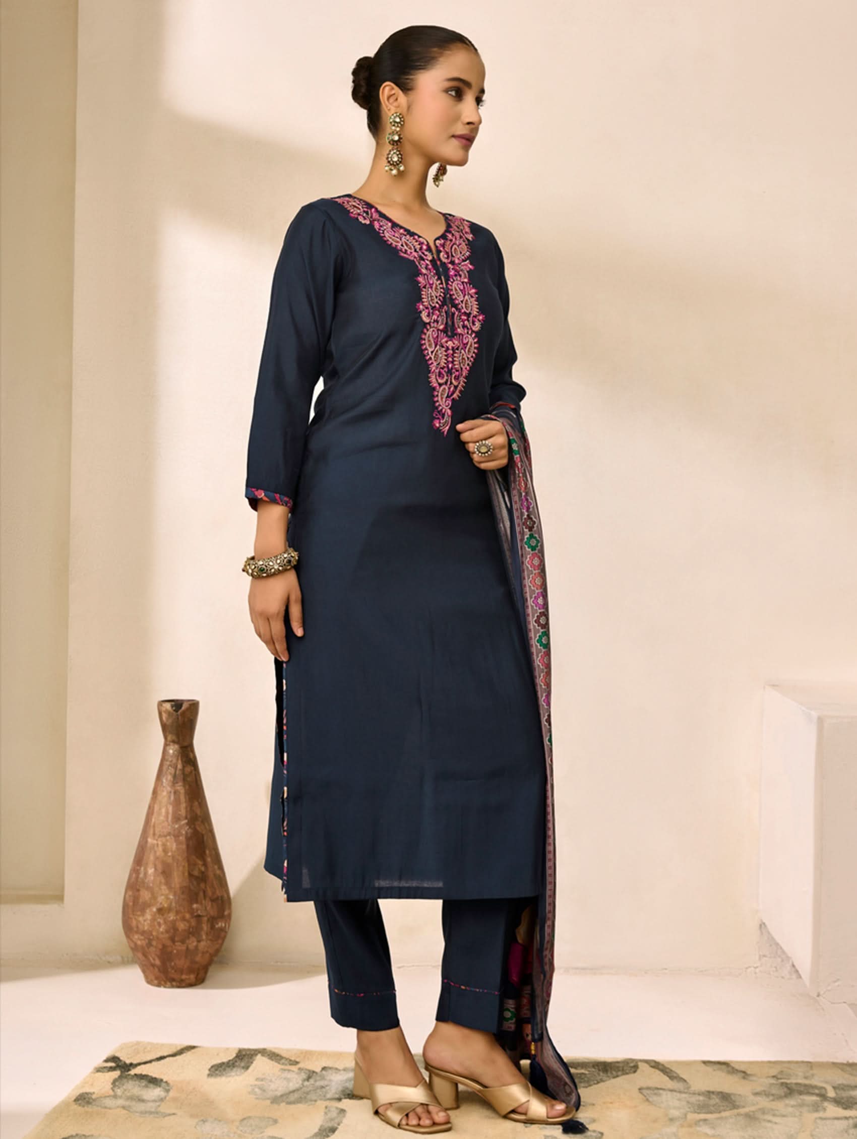 Woman wearing a navy blue kurta with pink embroidery in a minimalistic setting.